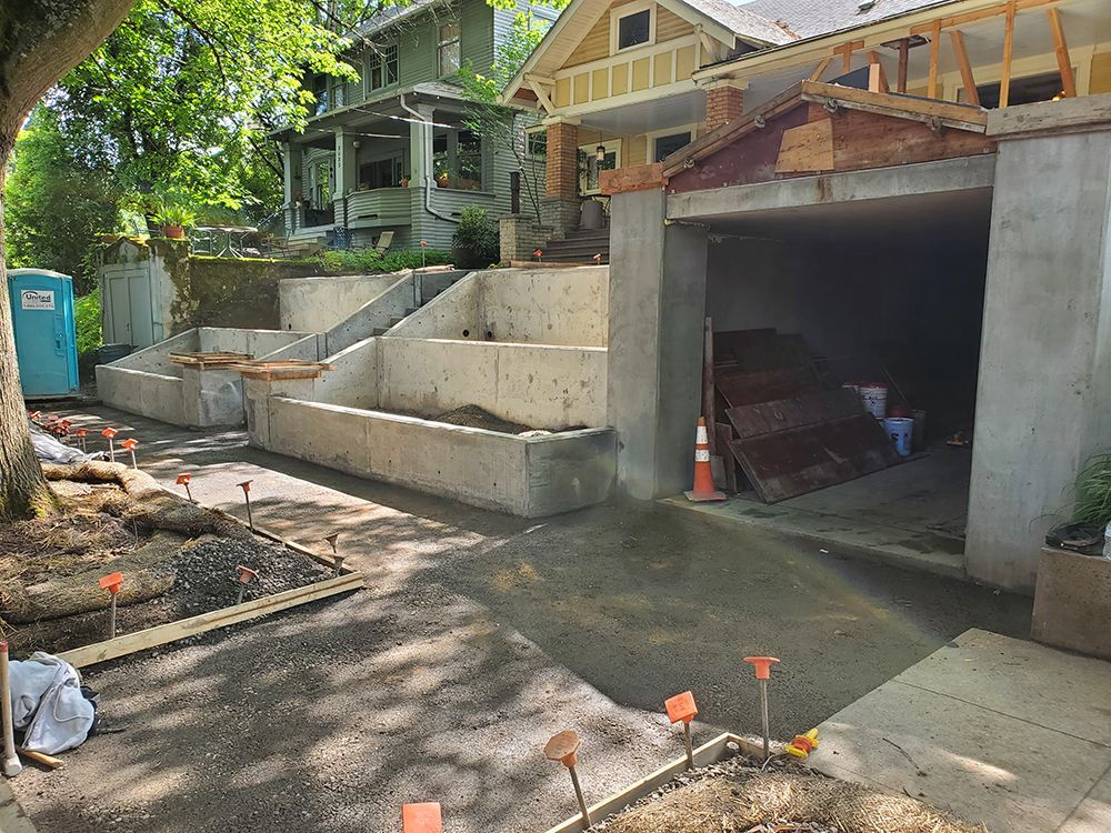Construction site with concrete retaining walls and garage; houses in background.