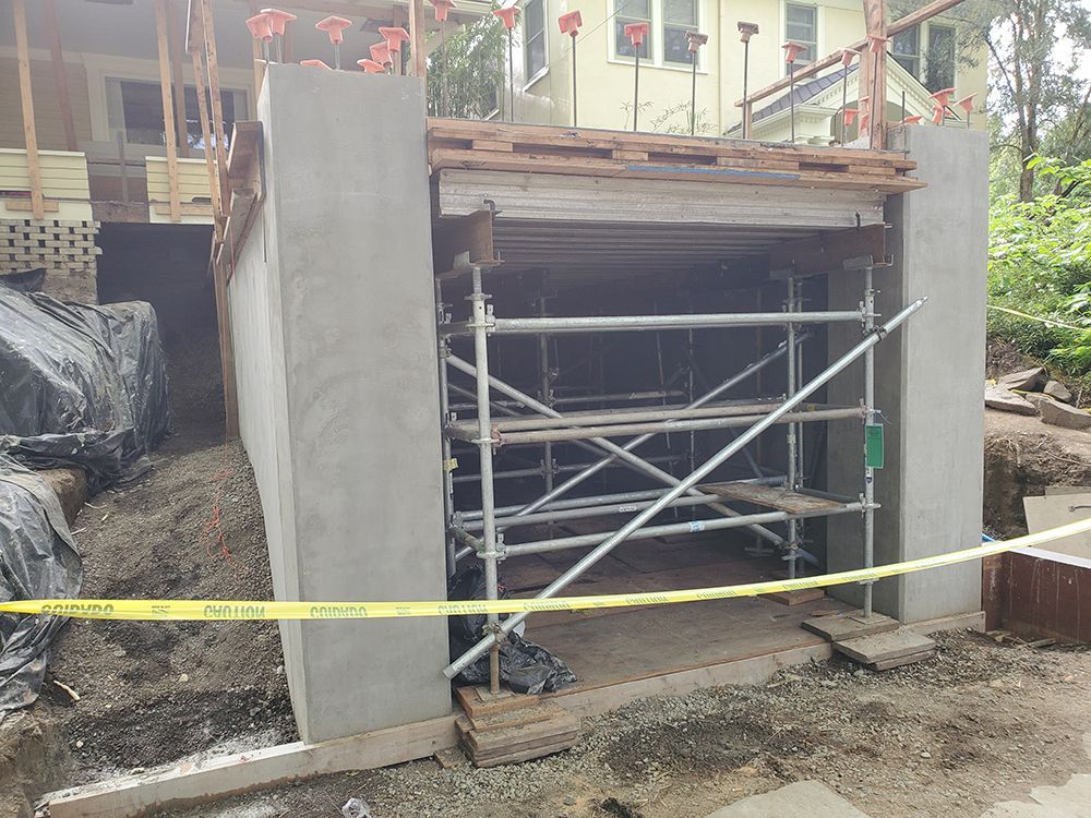 Construction site with concrete walls, scaffolding inside, yellow caution tape, and a wooden frame.