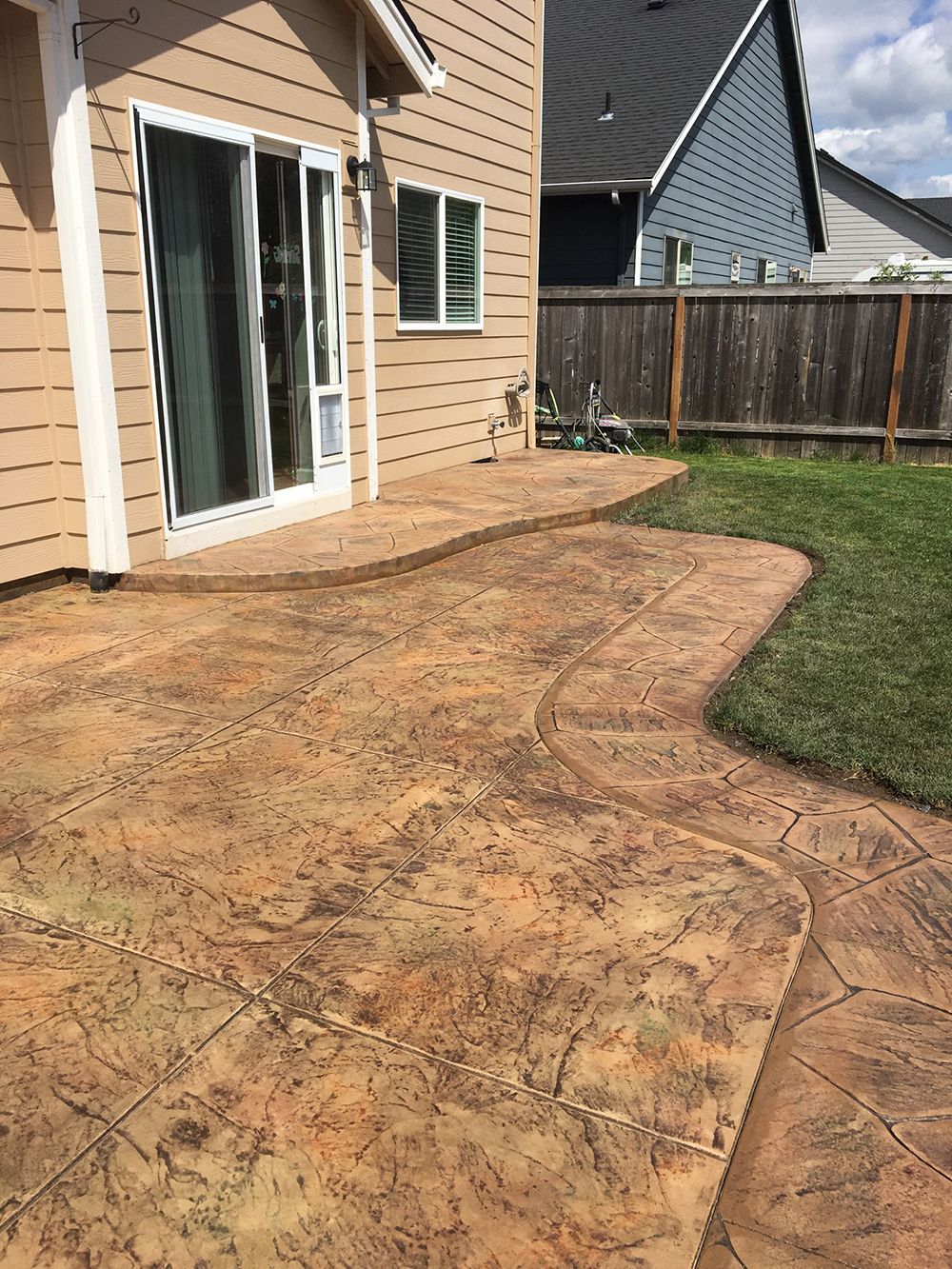 Stamped concrete patio with a tree-like pattern, next to a grassy lawn and a house.