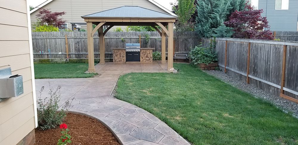 Backyard with a gazebo, grill, patio, and green lawn surrounded by a wooden fence.