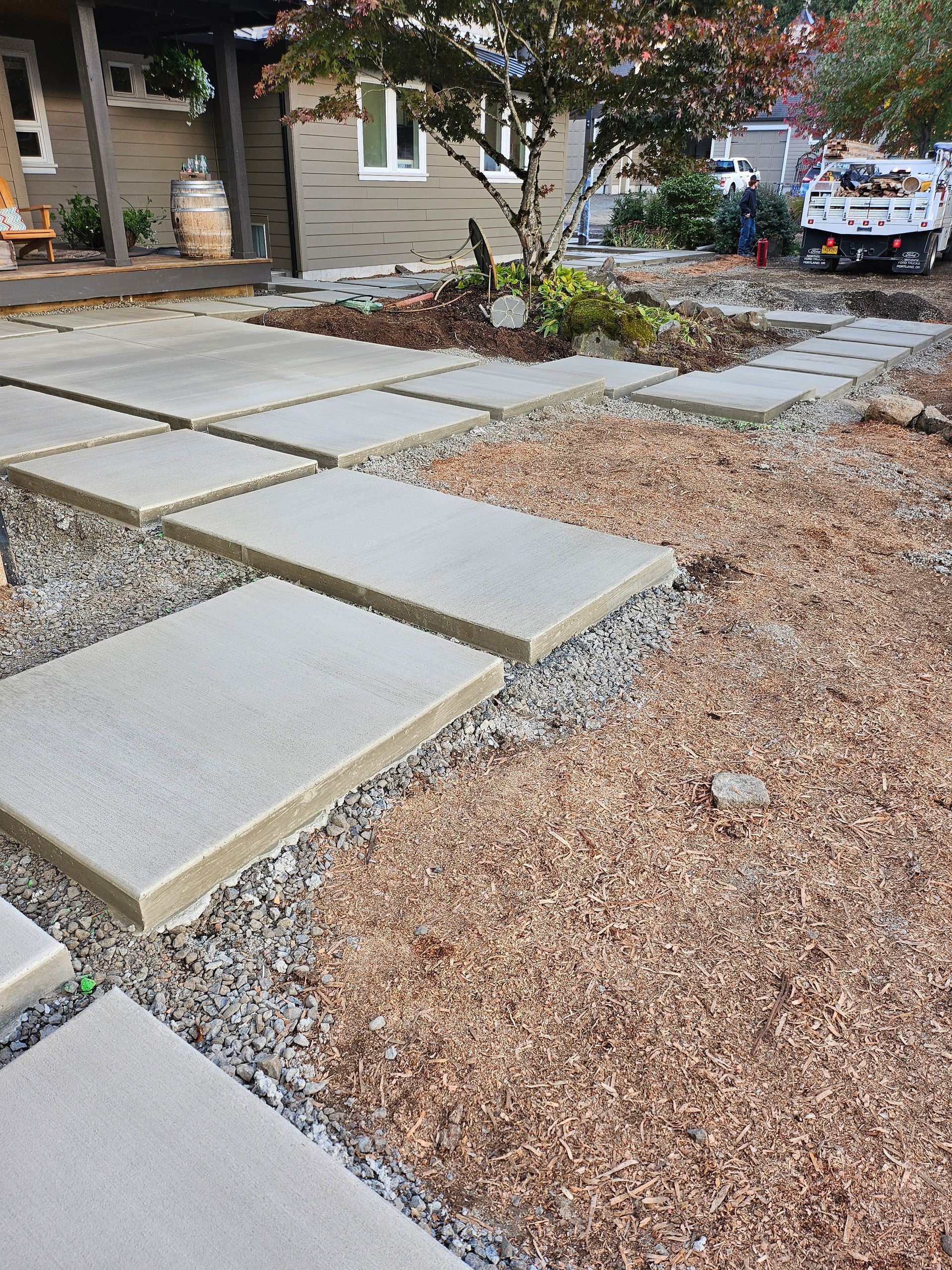 Concrete stepping stones on gravel path in front of a house, with a small tree in the center.