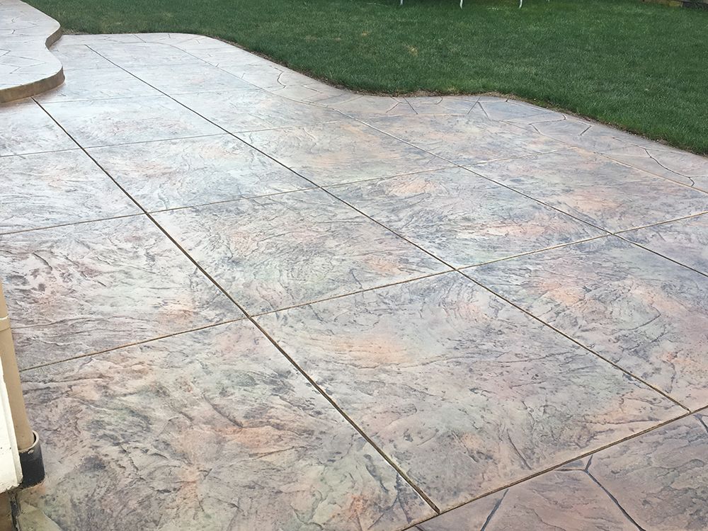 Stamped concrete patio with a textured pattern and color variations, next to a grassy lawn.