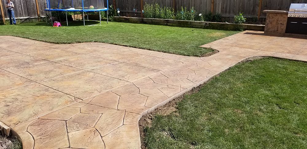 Backyard with stamped concrete patio and green lawn. A trampoline is visible.