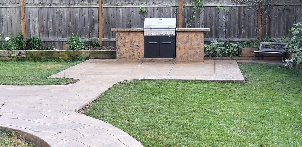 A backyard with a grill station on a concrete patio, grass lawn, and wooden fence.
