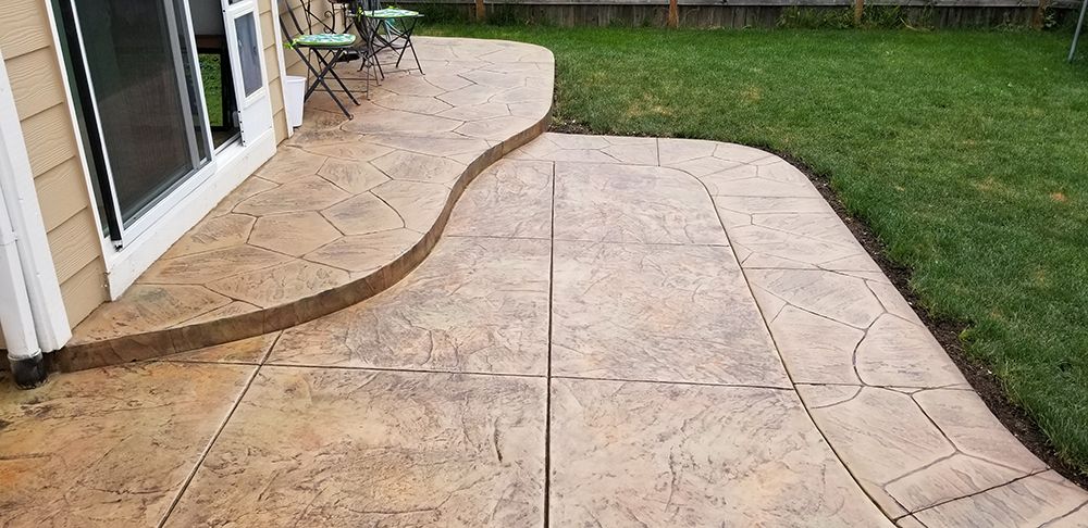 Stamped concrete patio with a curved edge next to a grassy lawn.