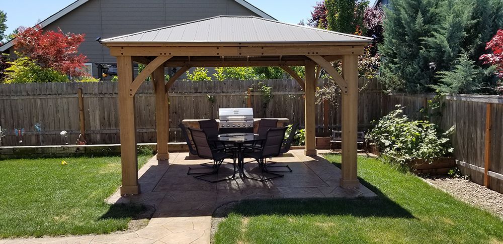 Wooden gazebo with a grill and table set in a backyard.