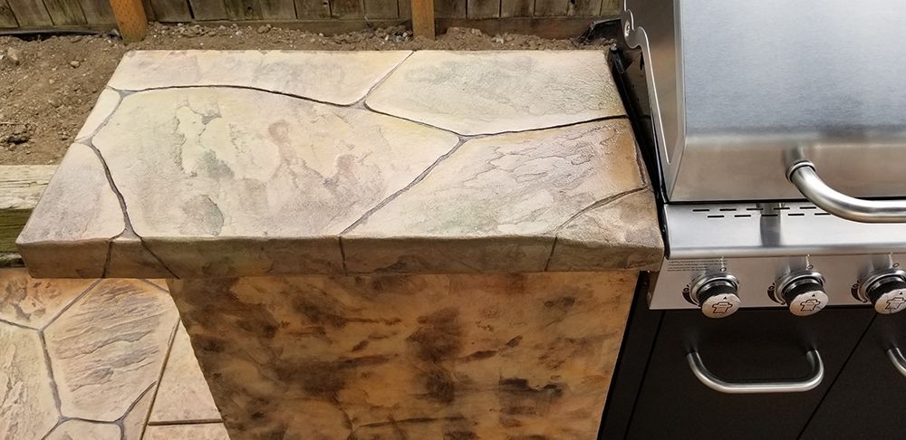 A stone-look countertop next to a stainless steel gas grill.