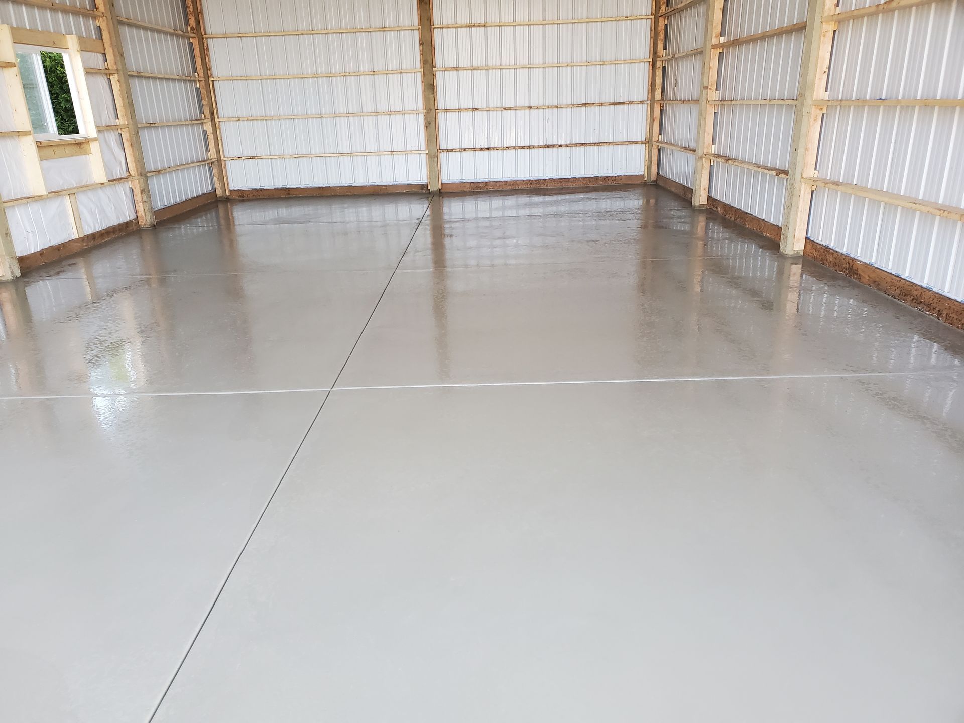 Inside a light-filled building with a smooth, gray concrete floor. Wood beams frame walls with white insulation.
