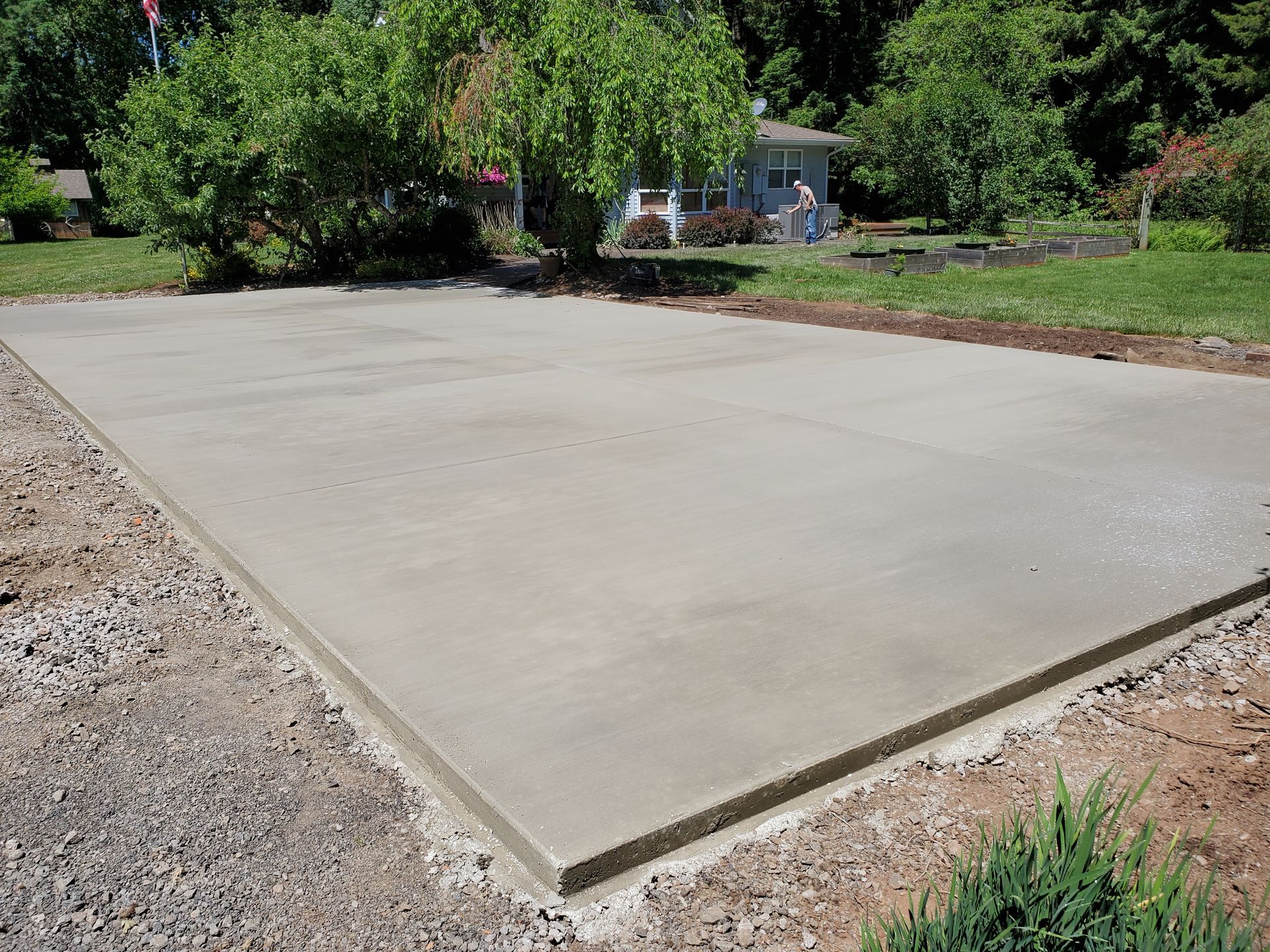 A newly poured concrete slab, surrounded by gravel, in a residential yard.