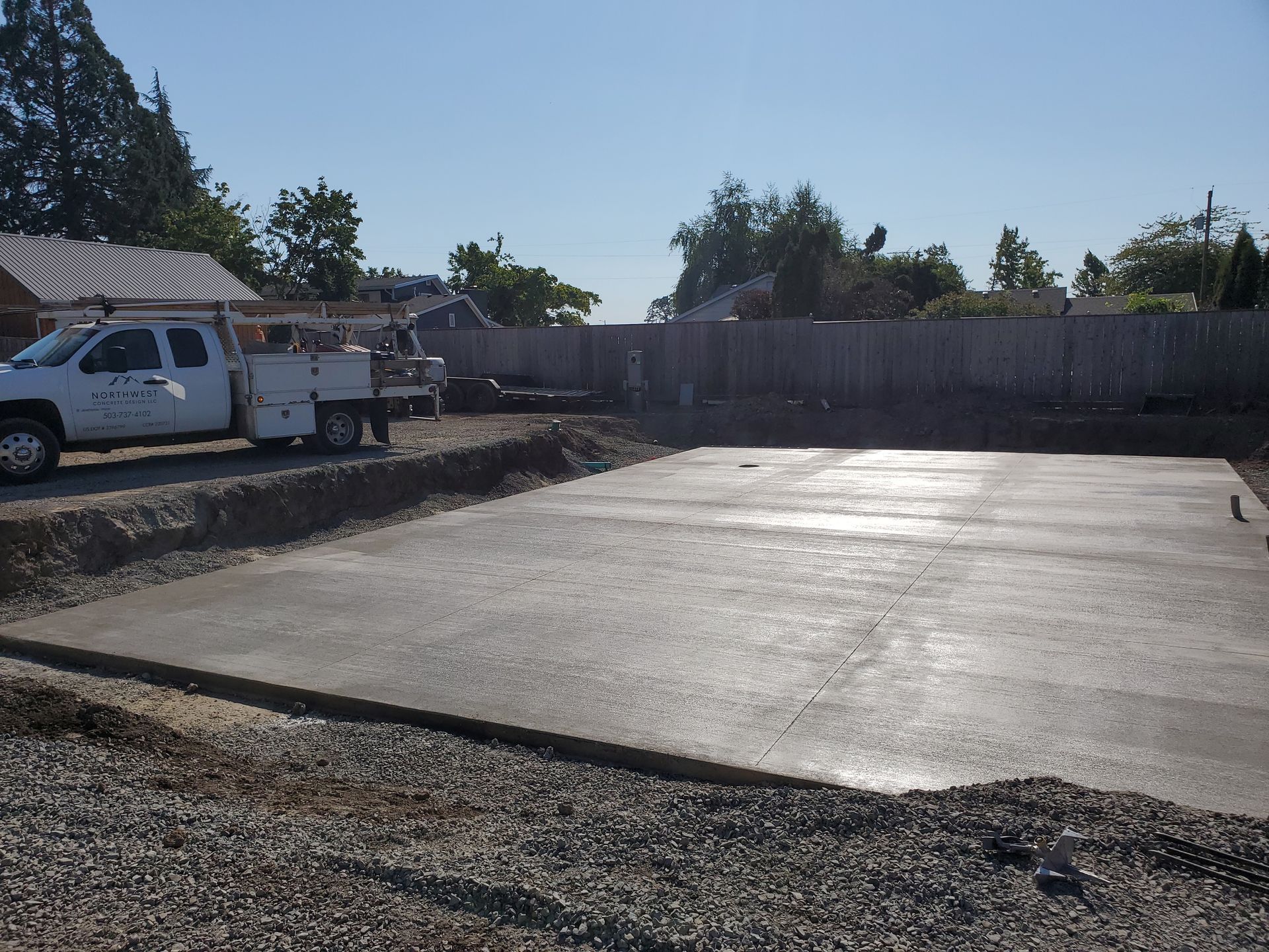 A freshly poured concrete foundation in a yard with a truck parked nearby.
