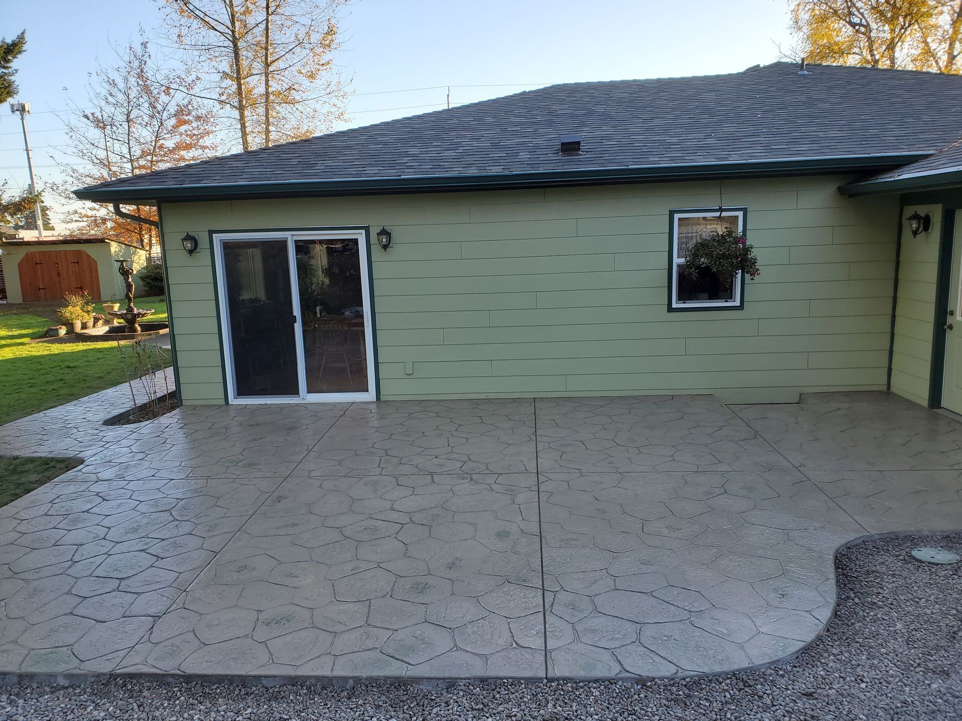 A concrete patio outside a light green house with a sliding door and a window.
