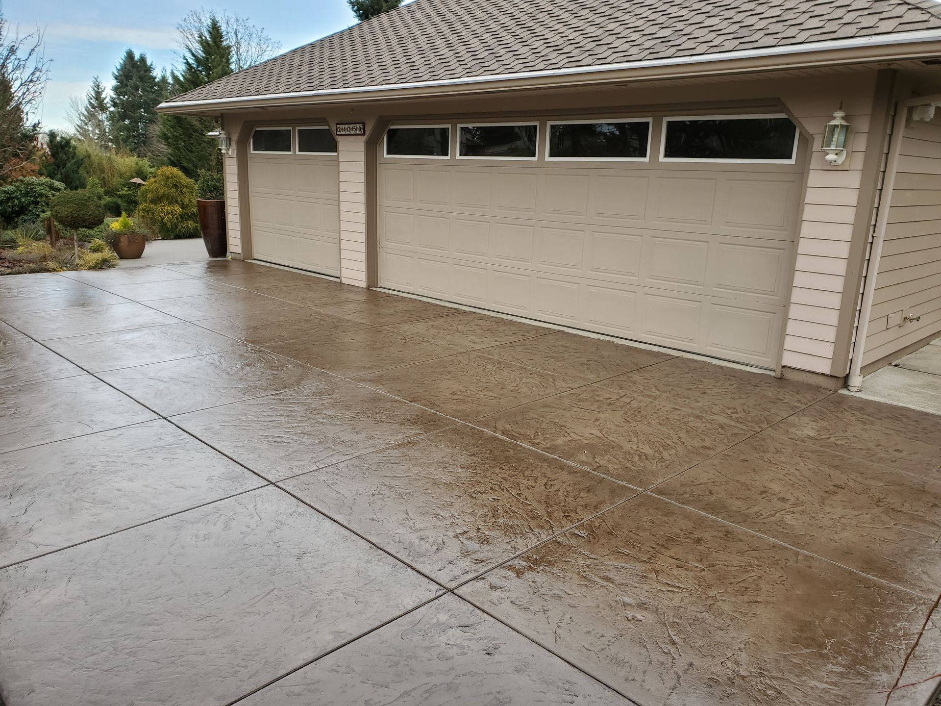 Wet, brown stamped concrete driveway in front of a tan garage with two doors and small windows above.