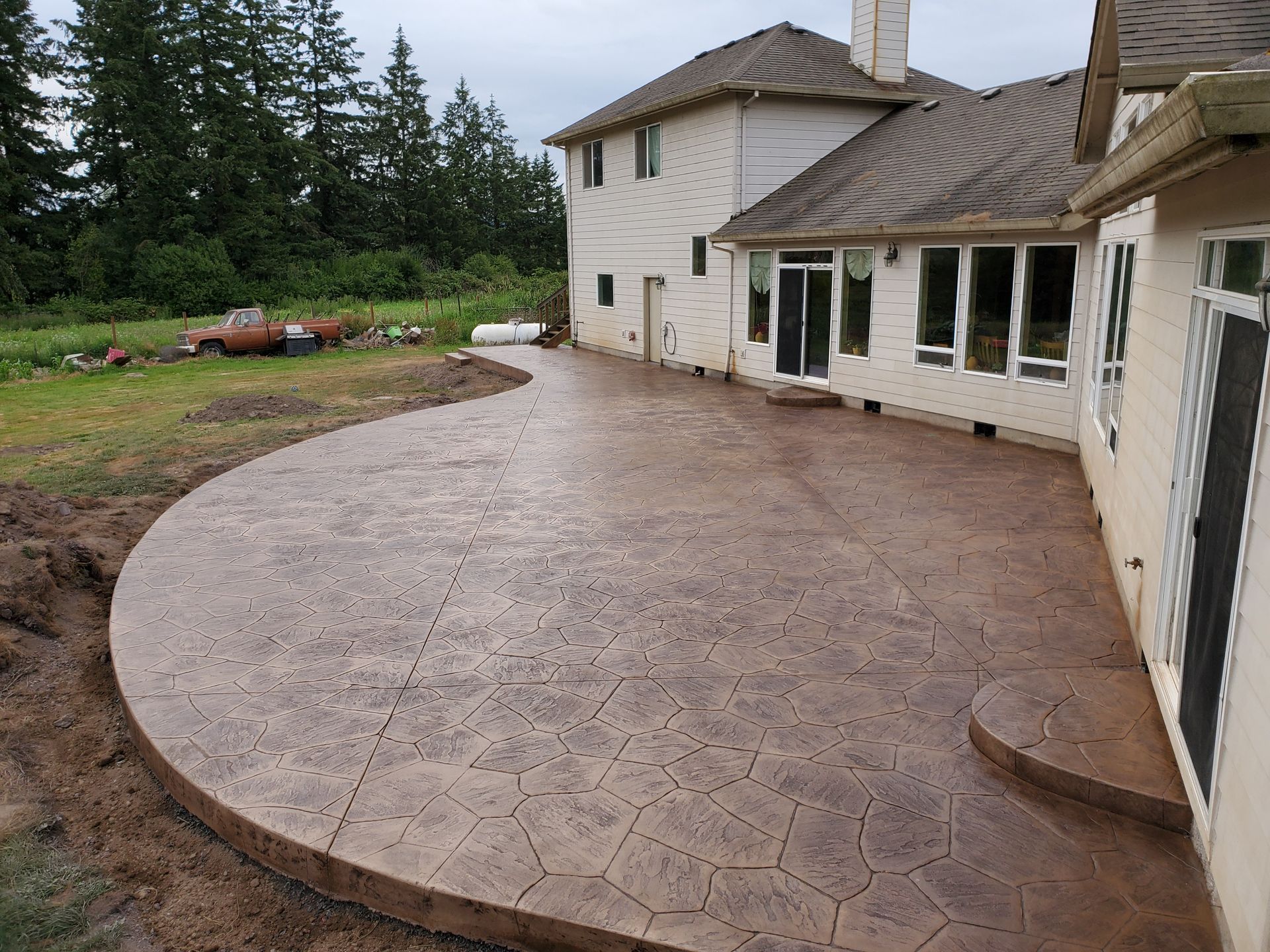 Brown stamped concrete patio next to a two-story house with trees in the background.