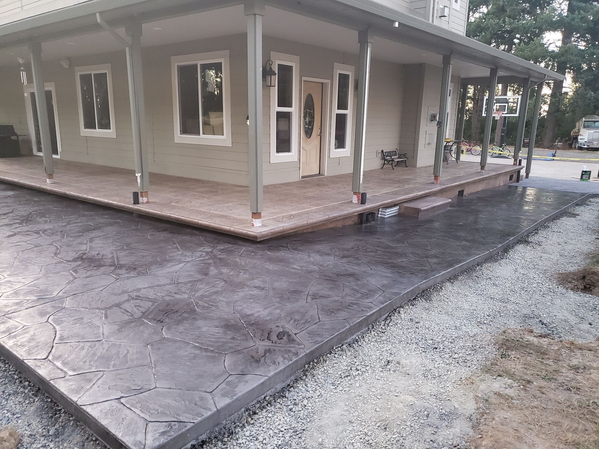 Stone-textured concrete patio and porch with house and gravel border.