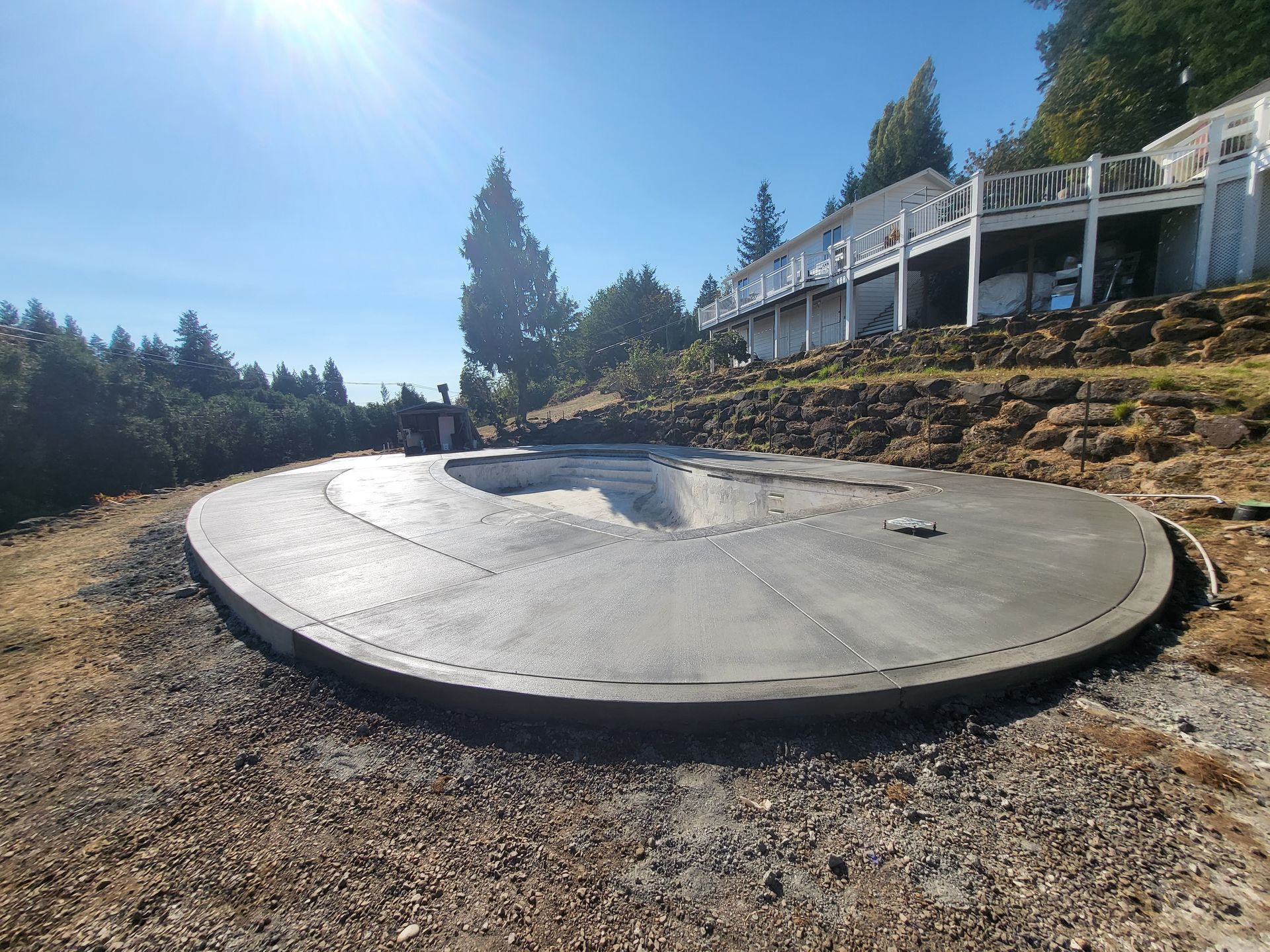Circular concrete patio, freshly poured, on a hillside. House in background.