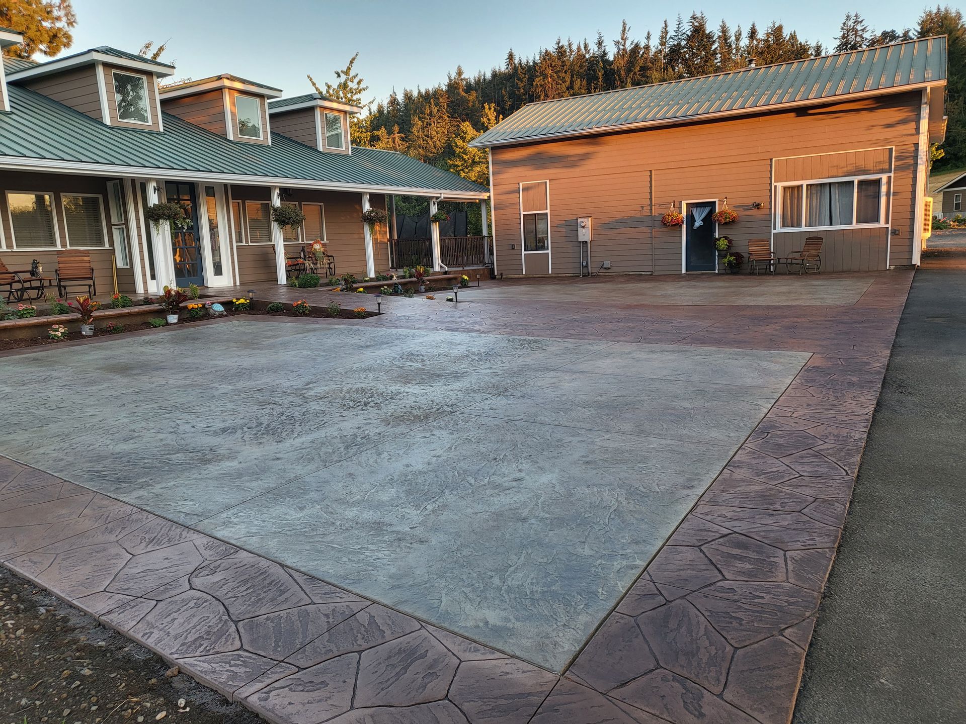 Exterior view: building with gray concrete patio and brown decorative border. Green roof, trees in background.