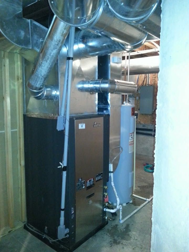 Large HVAC furnace and ductwork in a utility room with metal pipes and insulation.
