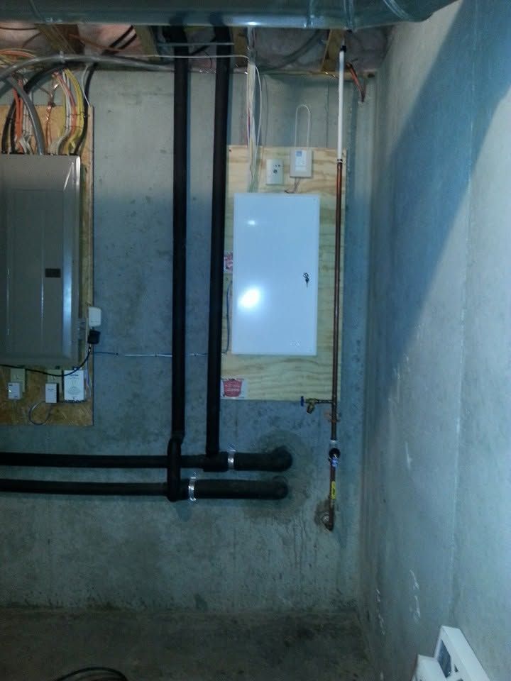 Basement utility room with electrical panel, exposed pipes, and unfinished concrete walls.