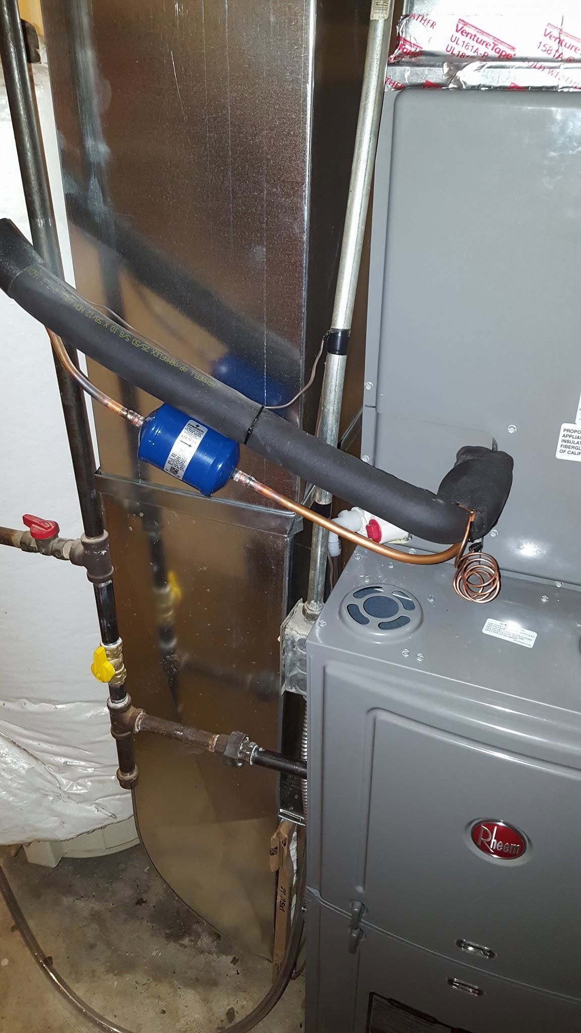 HVAC furnace with insulated ductwork, copper piping, and blue inline component in a utility closet