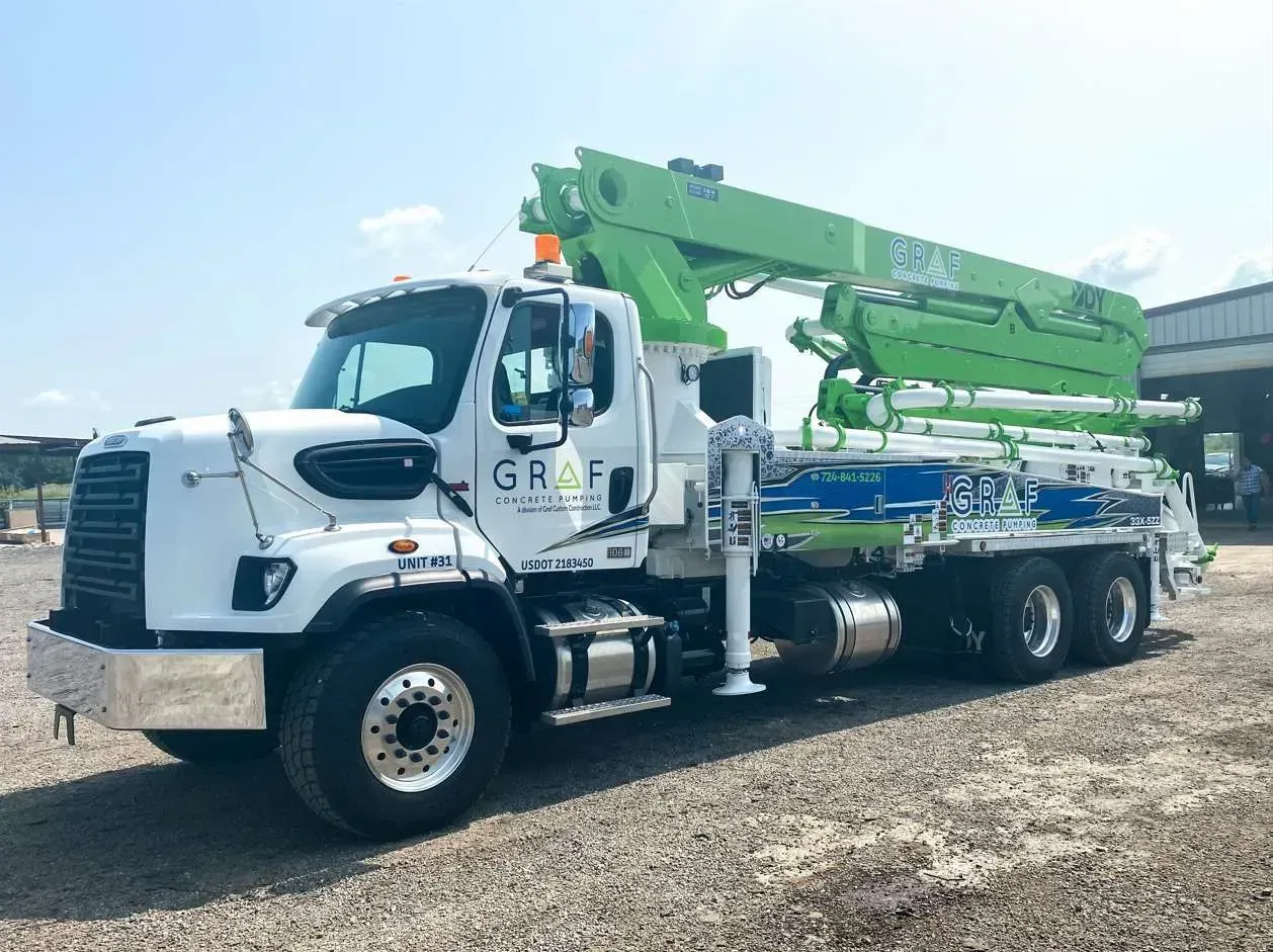 A white and bright green concrete pump truck parked on a gravel lot under a clear blue sky.