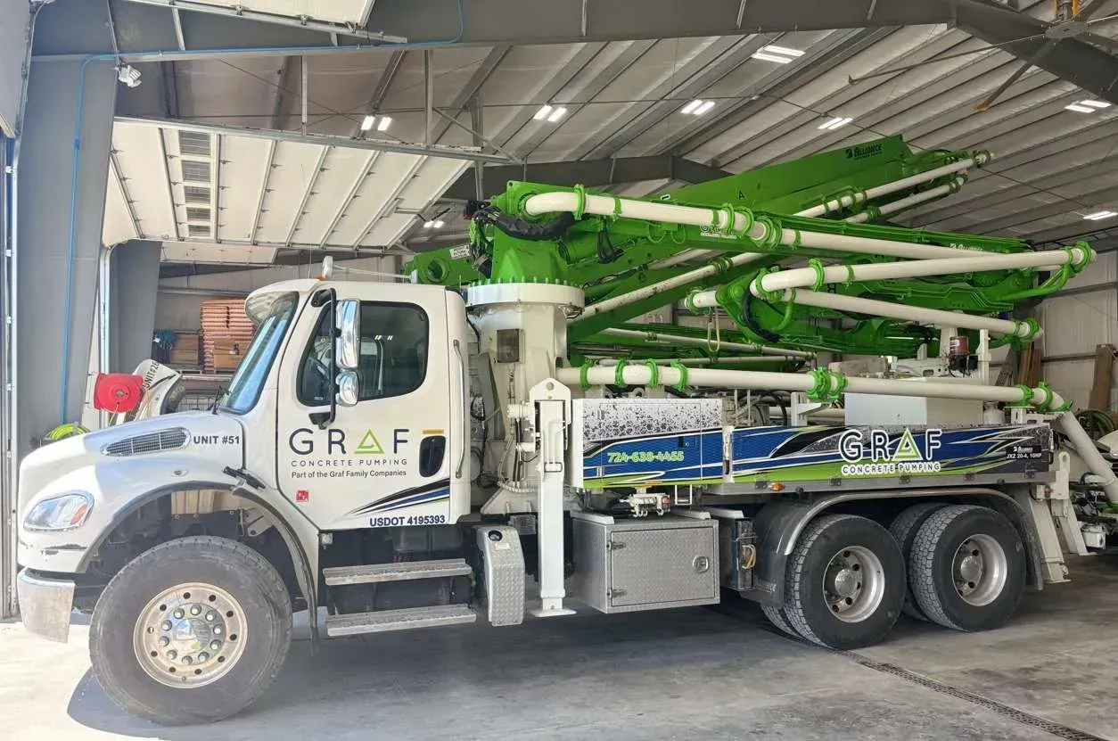 White Graf concrete pump truck with a folded lime green boom arm parked inside a warehouse.