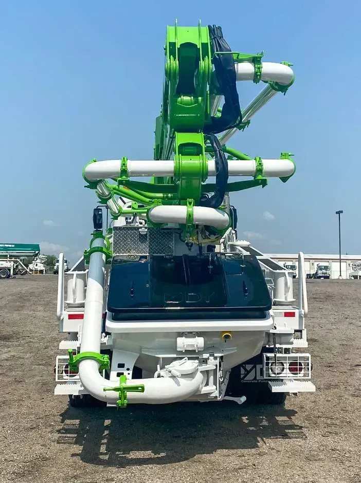 Rear view of a green and white concrete pump truck parked on a gravel lot under a clear blue sky.