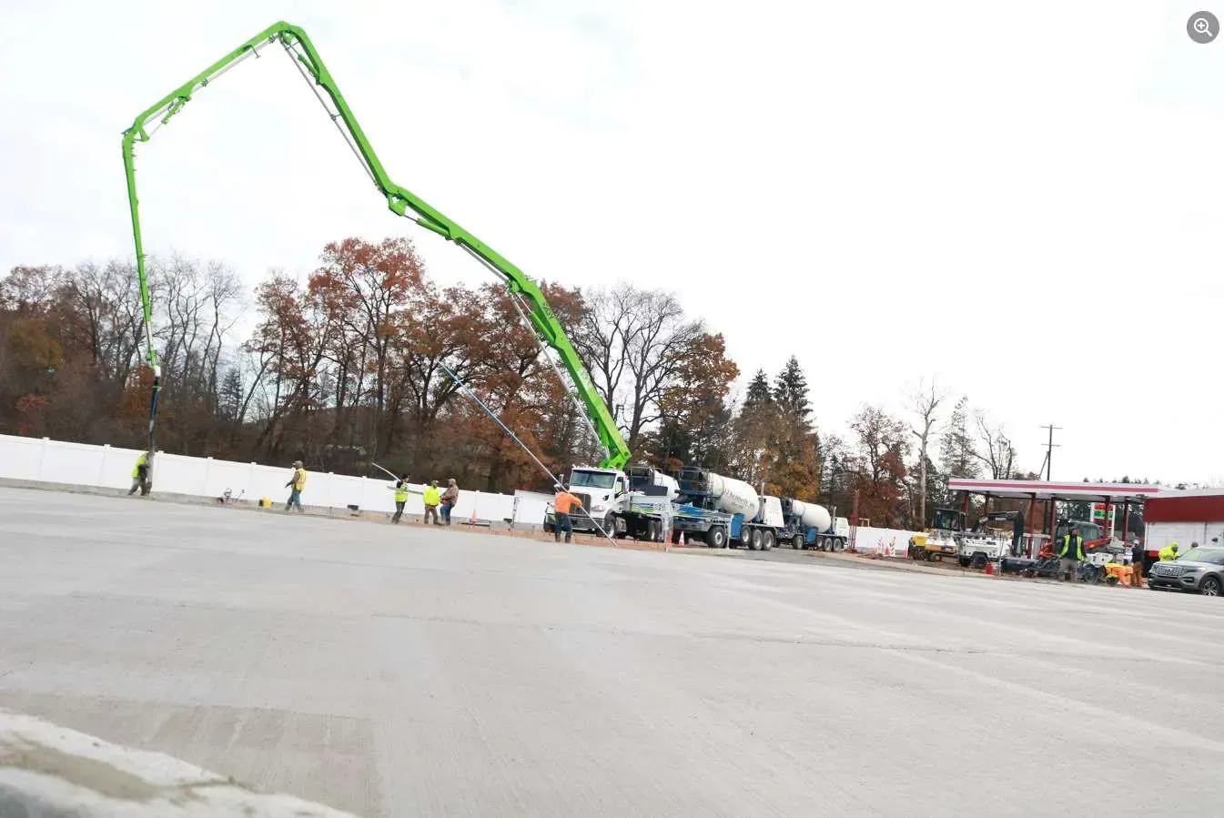 A large green concrete pump truck extends its boom over a construction site with workers nearby.