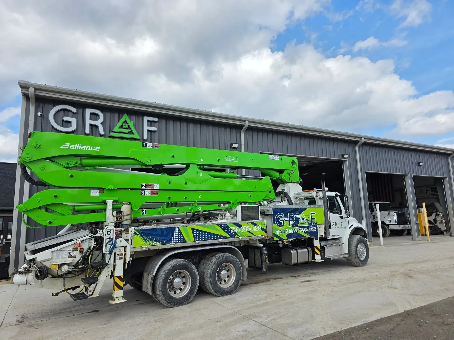 A bright green concrete pump truck parked in front of a GRAF facility on a cloudy day.