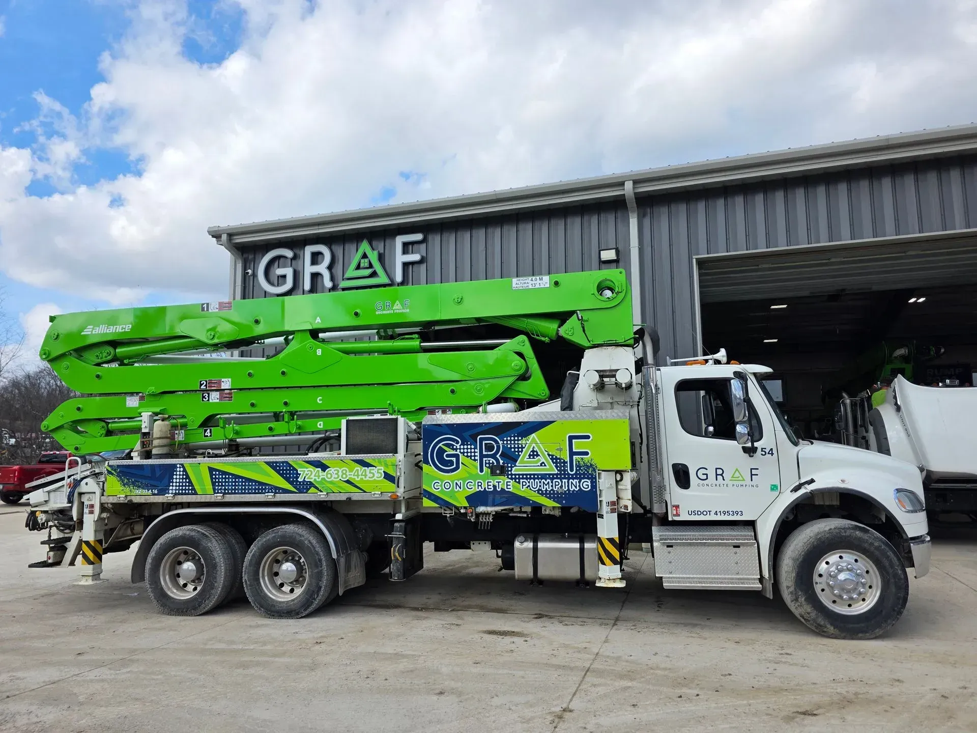 A bright green and white concrete pump truck parked outside a metal building with a 