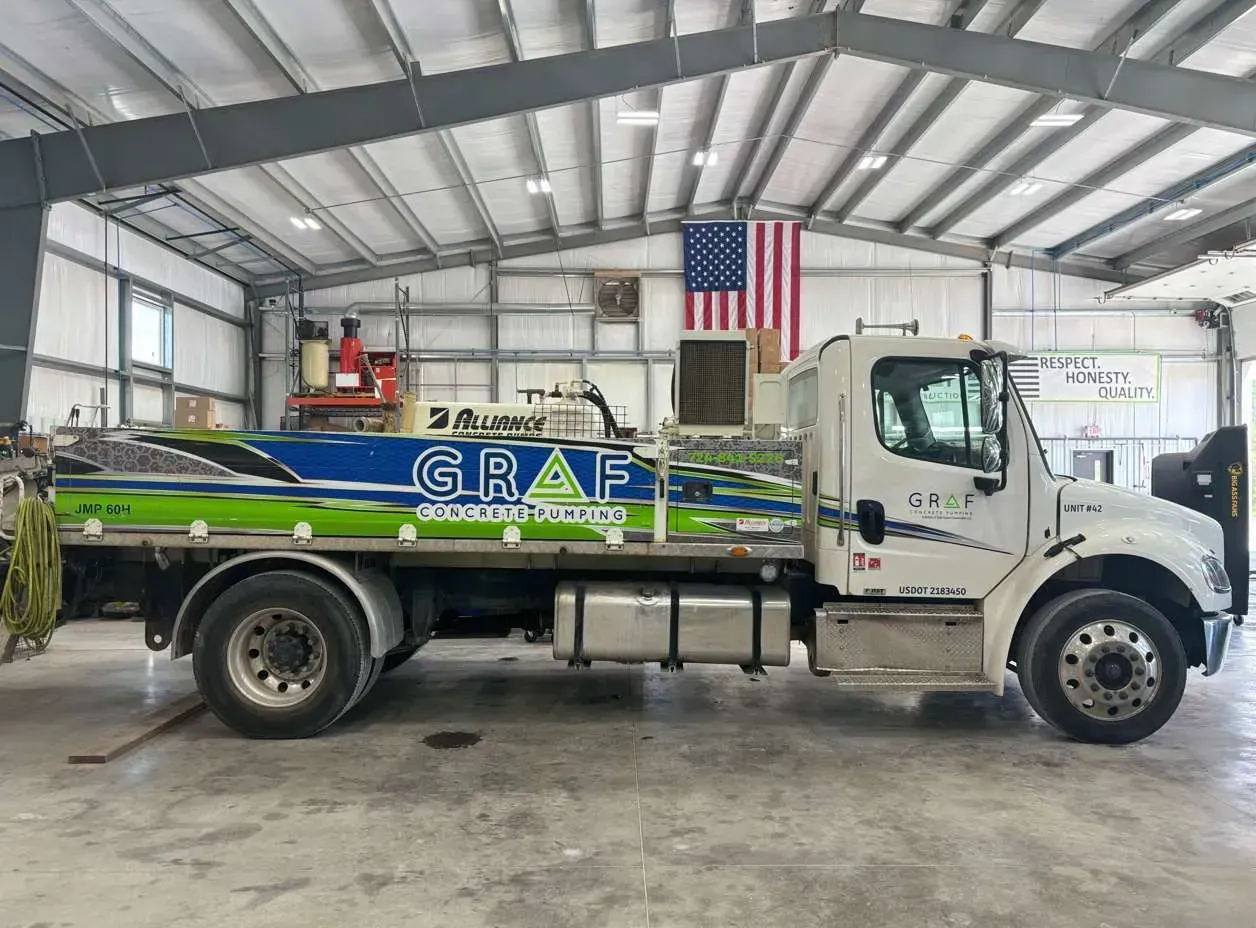 A white Graf commercial utility truck parked inside a large, open-bay warehouse beneath a hanging American flag.