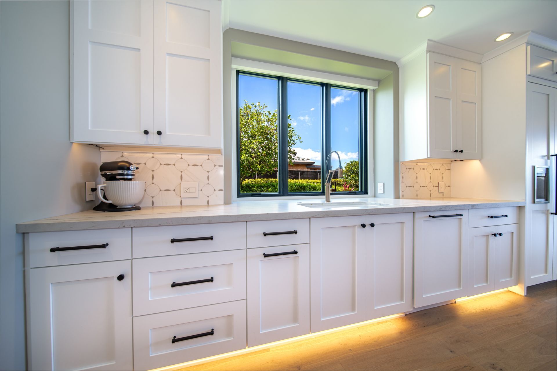 A kitchen with white cabinets and a large window.