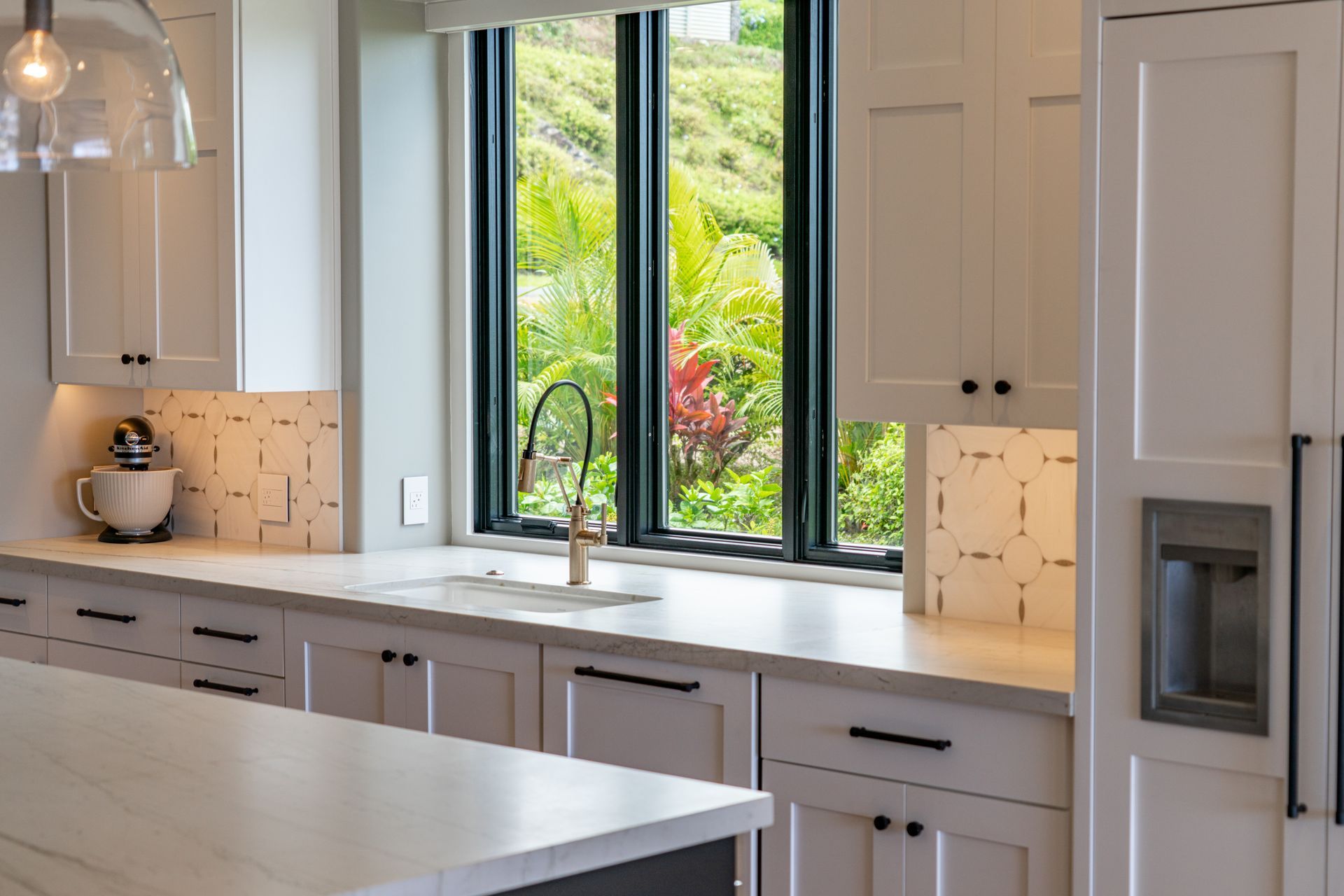 A kitchen with white cabinets , a sink , a refrigerator , and a large window.