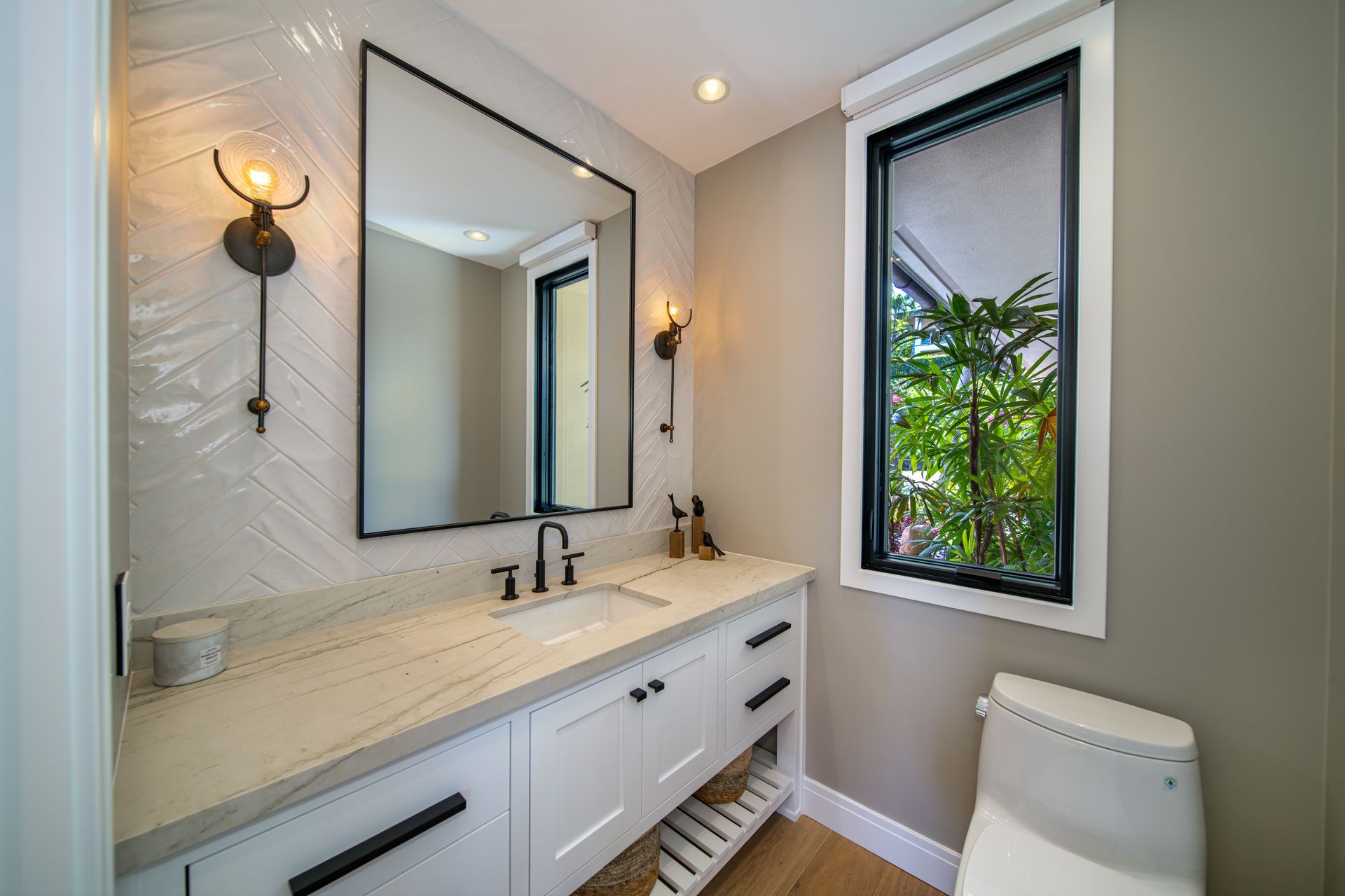 A bathroom with a sink , toilet , mirror and window.