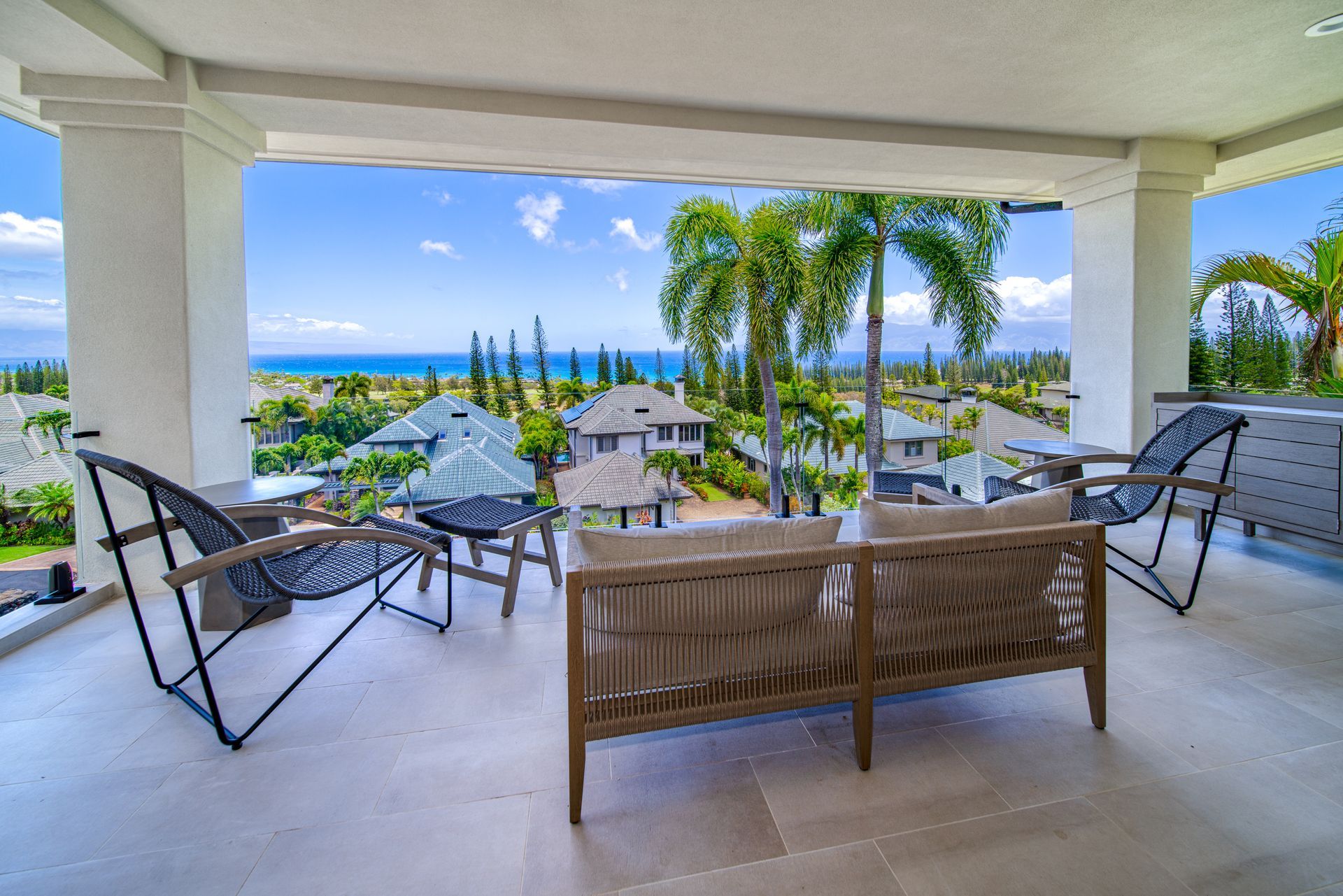 A balcony with a view of the ocean and a couch and chairs.