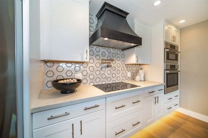 A kitchen with white cabinets , stainless steel appliances , and a black hood.