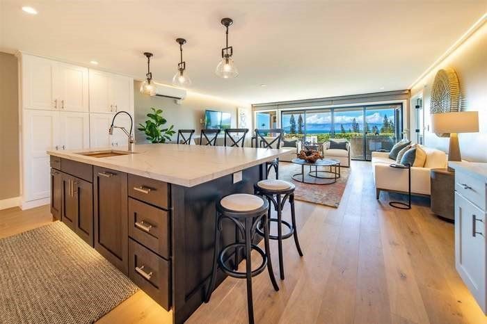 A kitchen with a large island and stools in a living room.