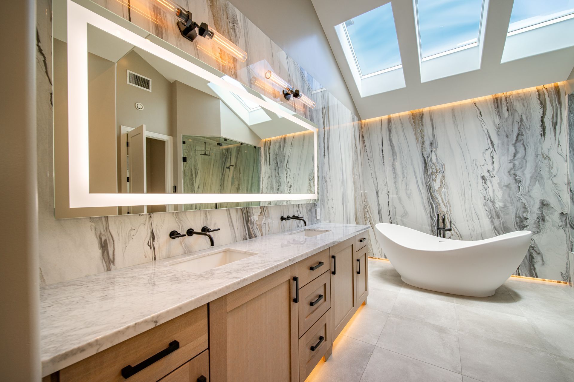 A bathroom with a bathtub , sinks , mirrors and skylights.