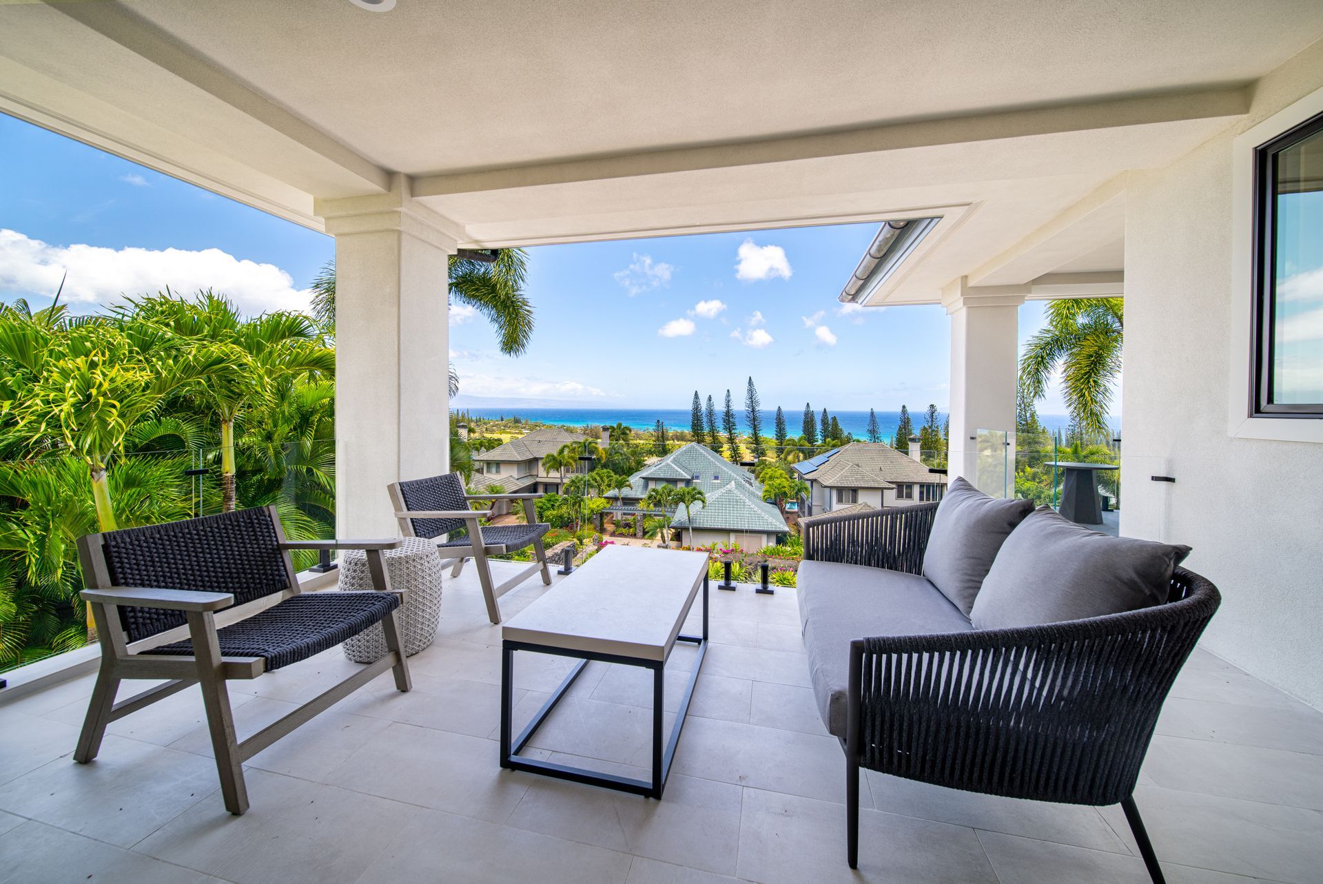 A patio with a couch , chairs and a table with a view of the ocean
