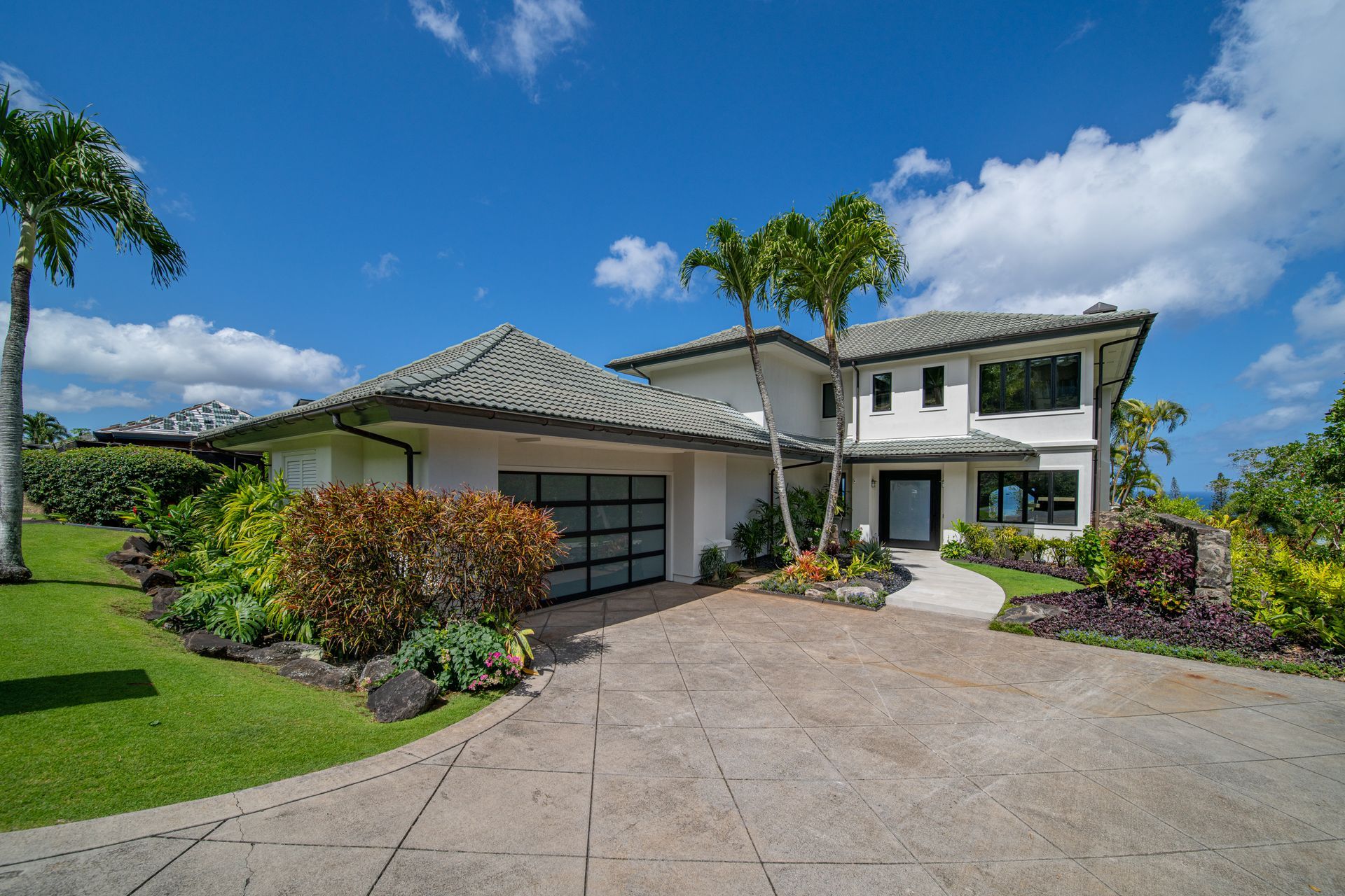 A large white house with a driveway and palm trees in front of it.