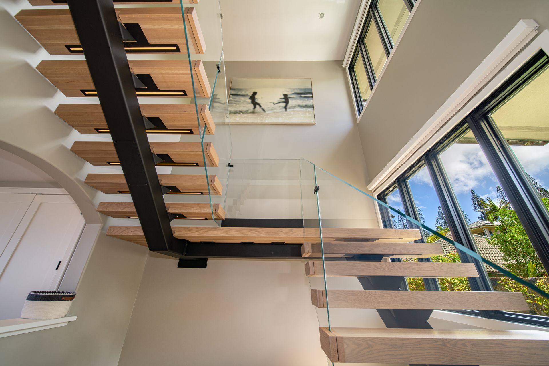 A wooden staircase with a glass railing and a painting on the wall.