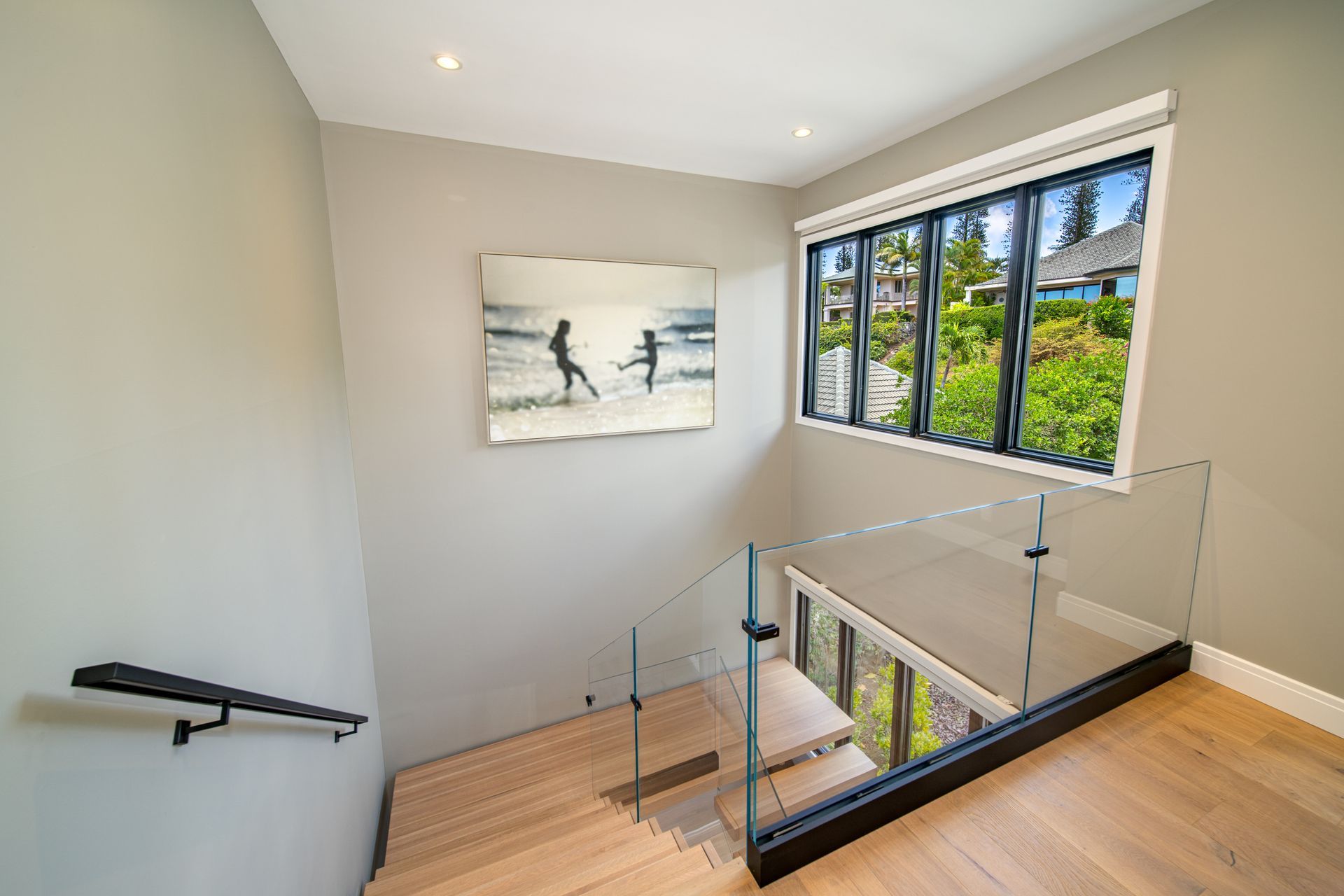 A staircase with a glass railing and a painting on the wall.