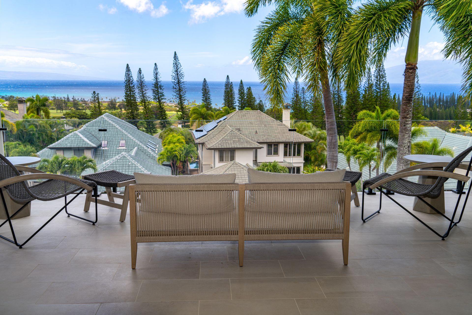 There is a couch and chairs on the balcony with a view of the ocean.