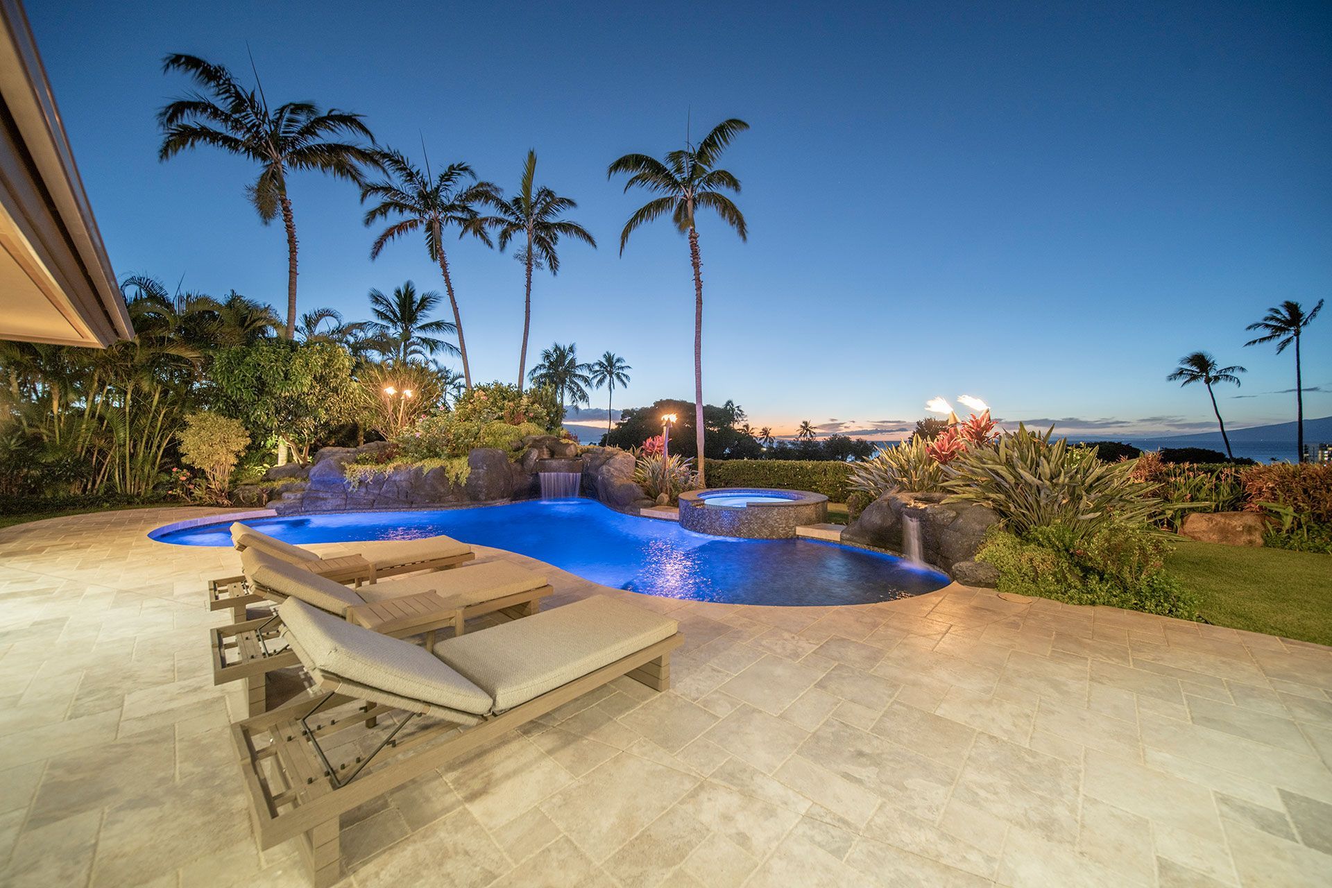 There is a large swimming pool in the backyard of a house with palm trees in the background