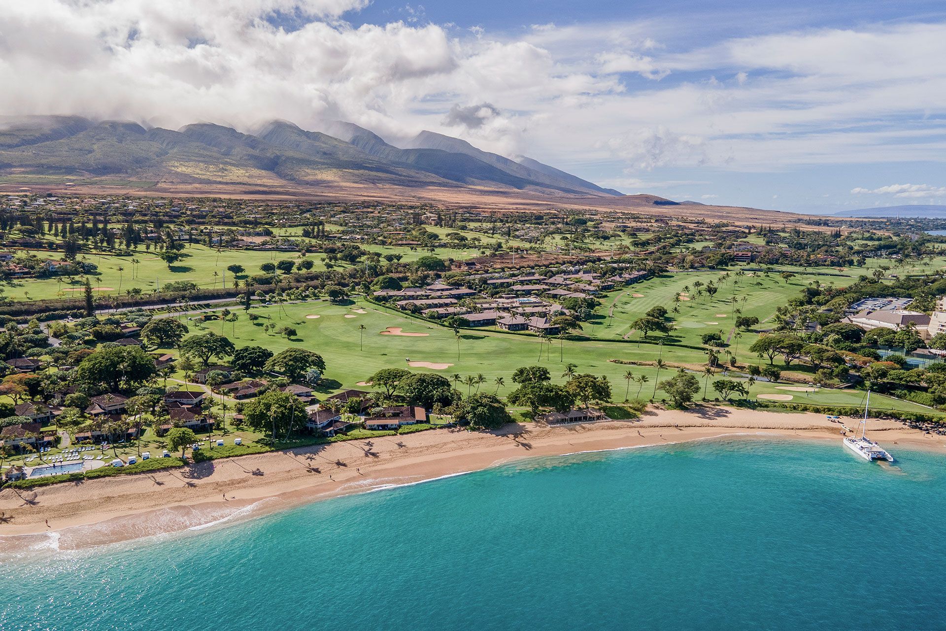 An aerial view of a beach with a golf course and mountains in the background