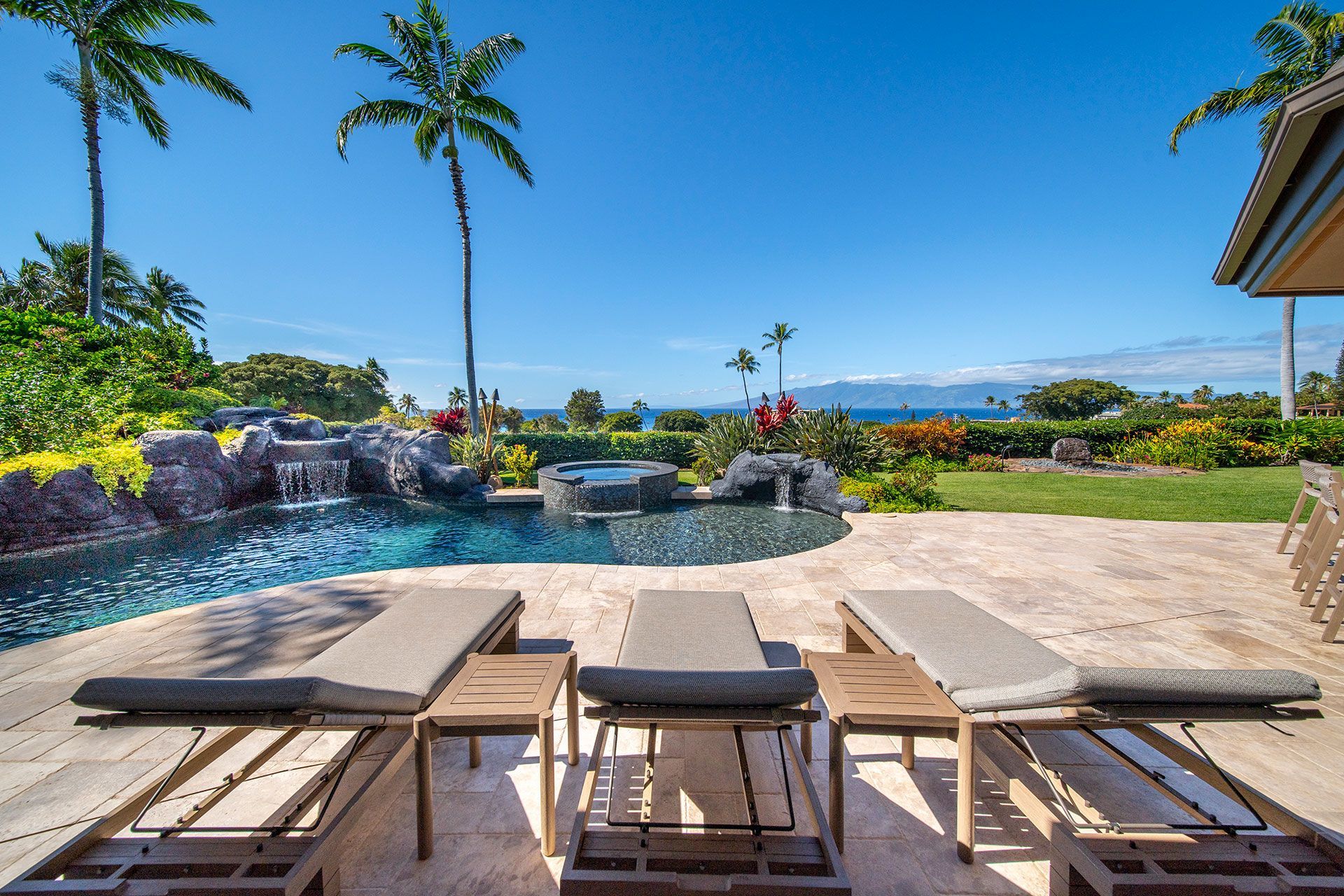 A patio with lounge chairs and a pool with palm trees in the background