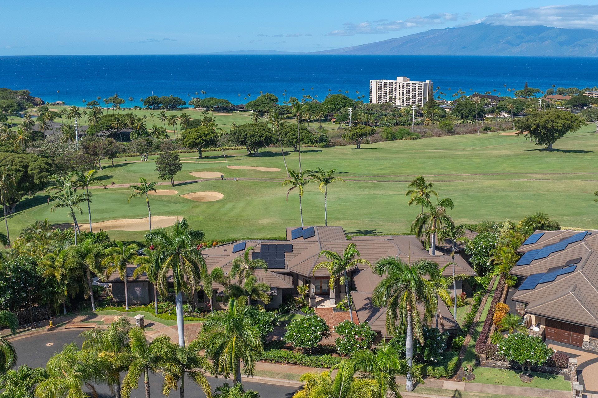 An aerial view of a house with a golf course in the background and the ocean in the background