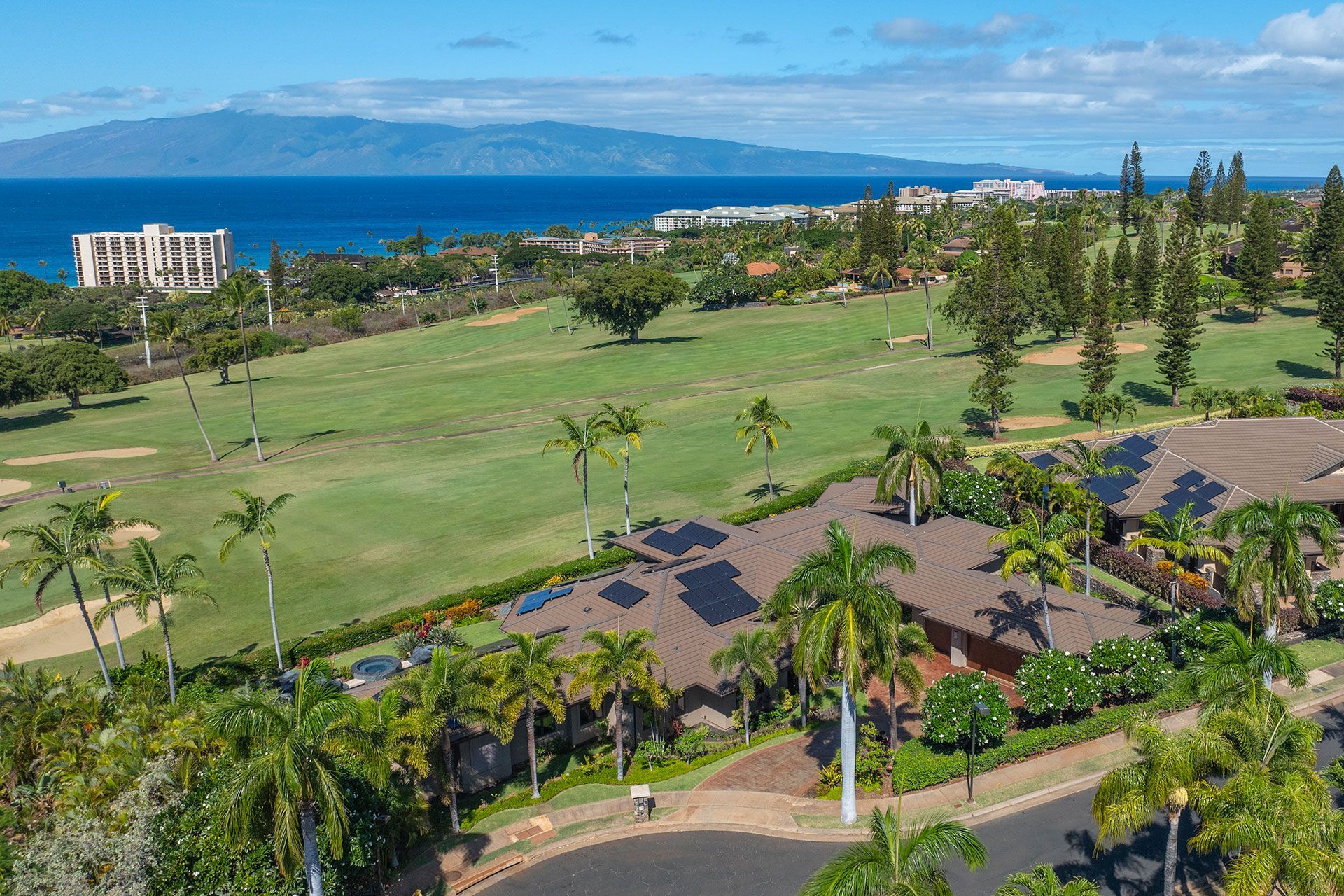 An aerial view of a house surrounded by palm trees and a golf course