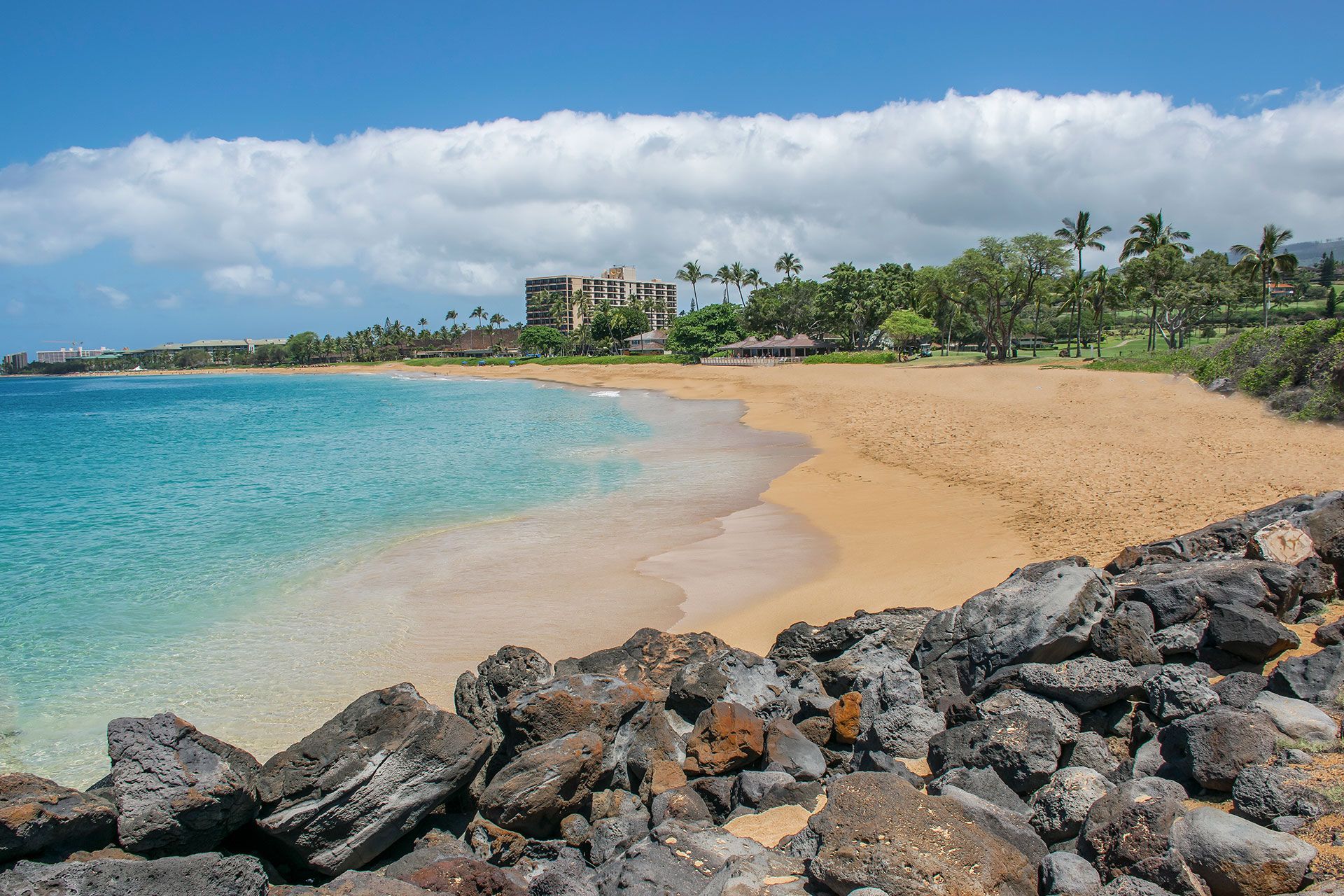 A beach with a building in the background and rocks in the foreground