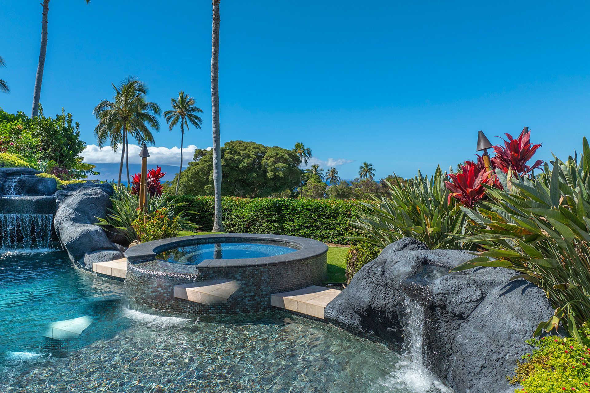 A swimming pool with a hot tub and a waterfall in the background