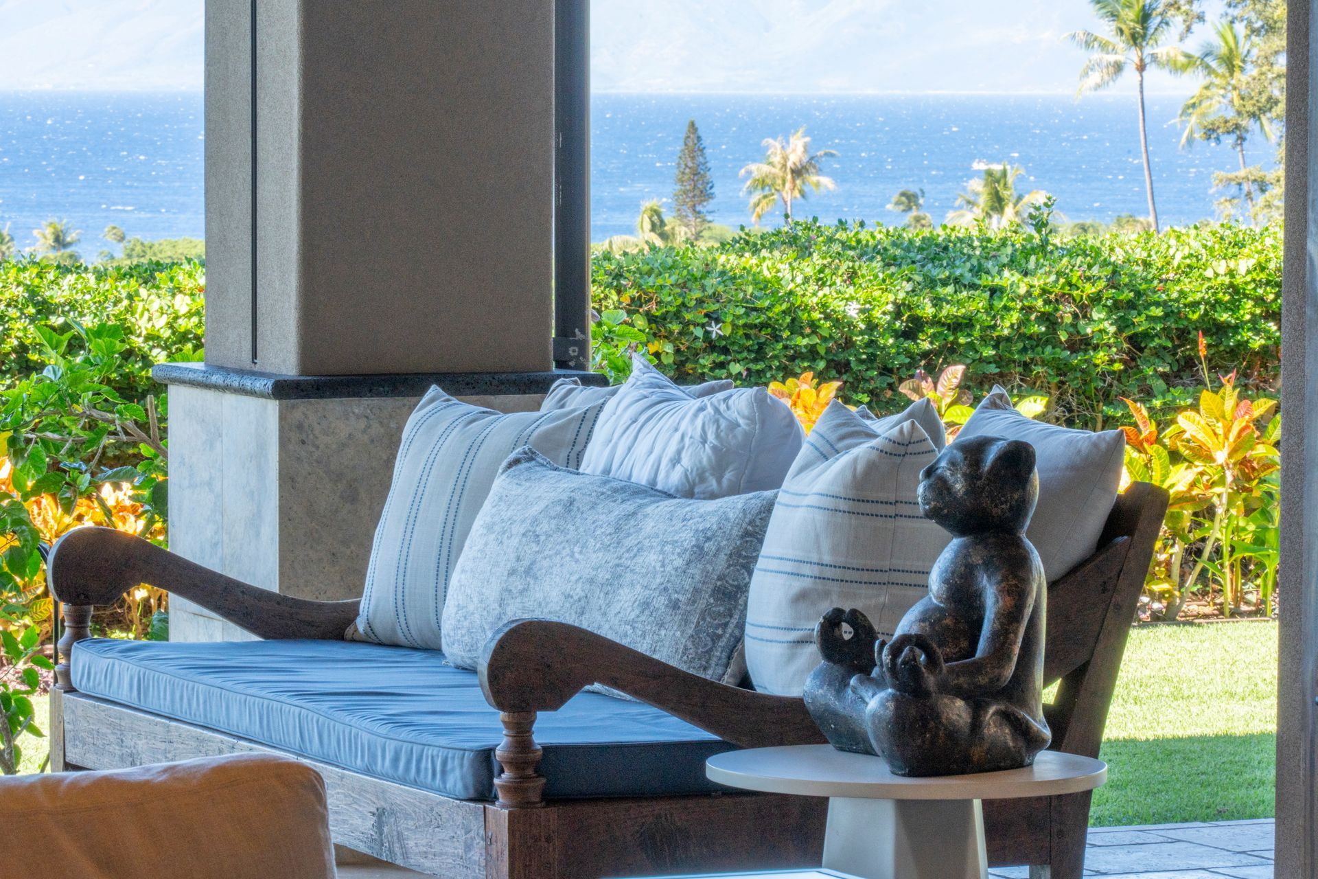 A couch with a statue of a monkey on it is sitting on a porch overlooking the ocean.